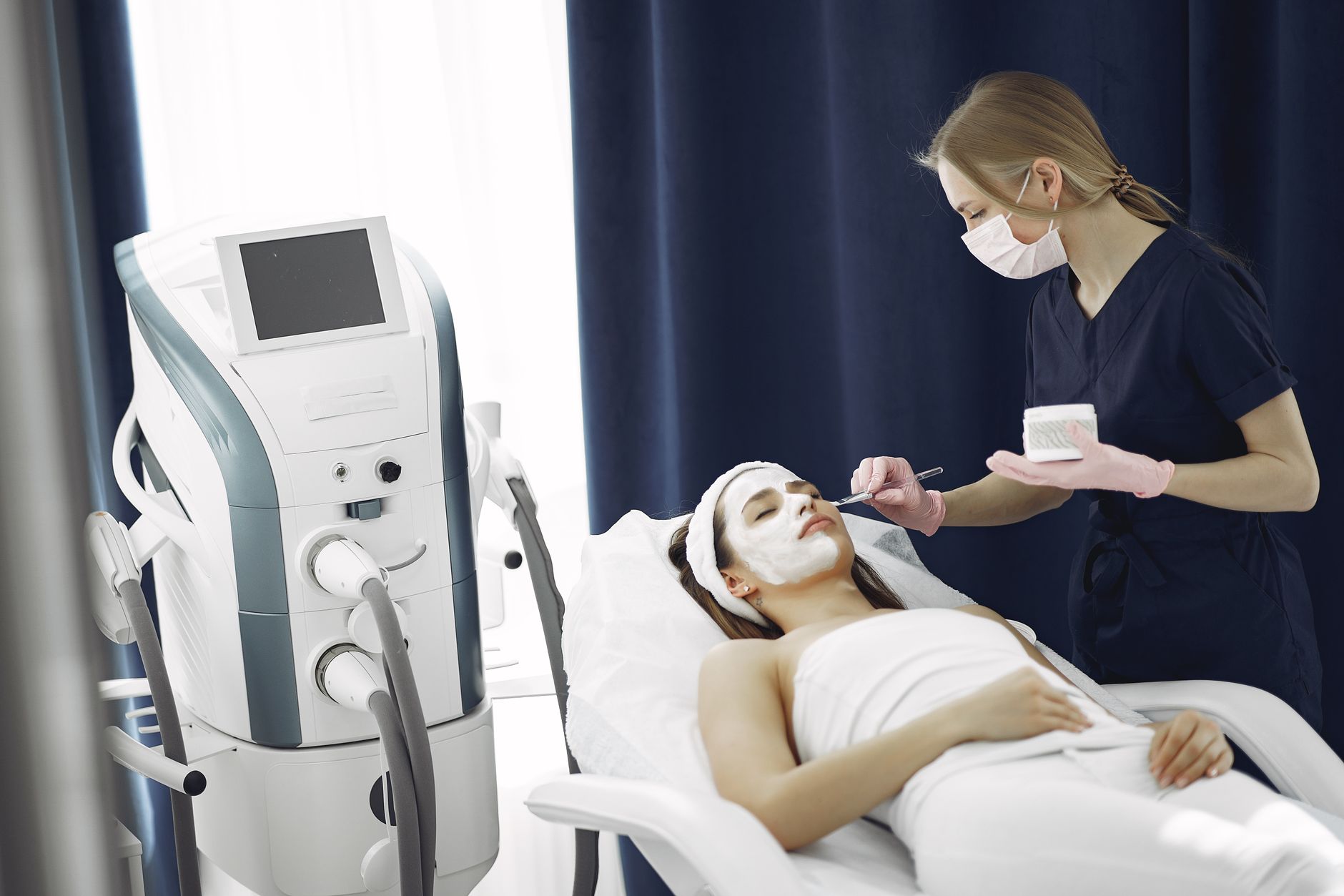 A beautician applies a facial mask on a client's face in a spa.