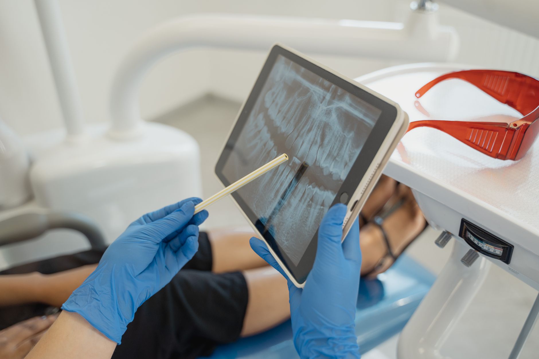 A dentist reviewing an X-ray on a tablet while a patient relaxes in a dental chair.