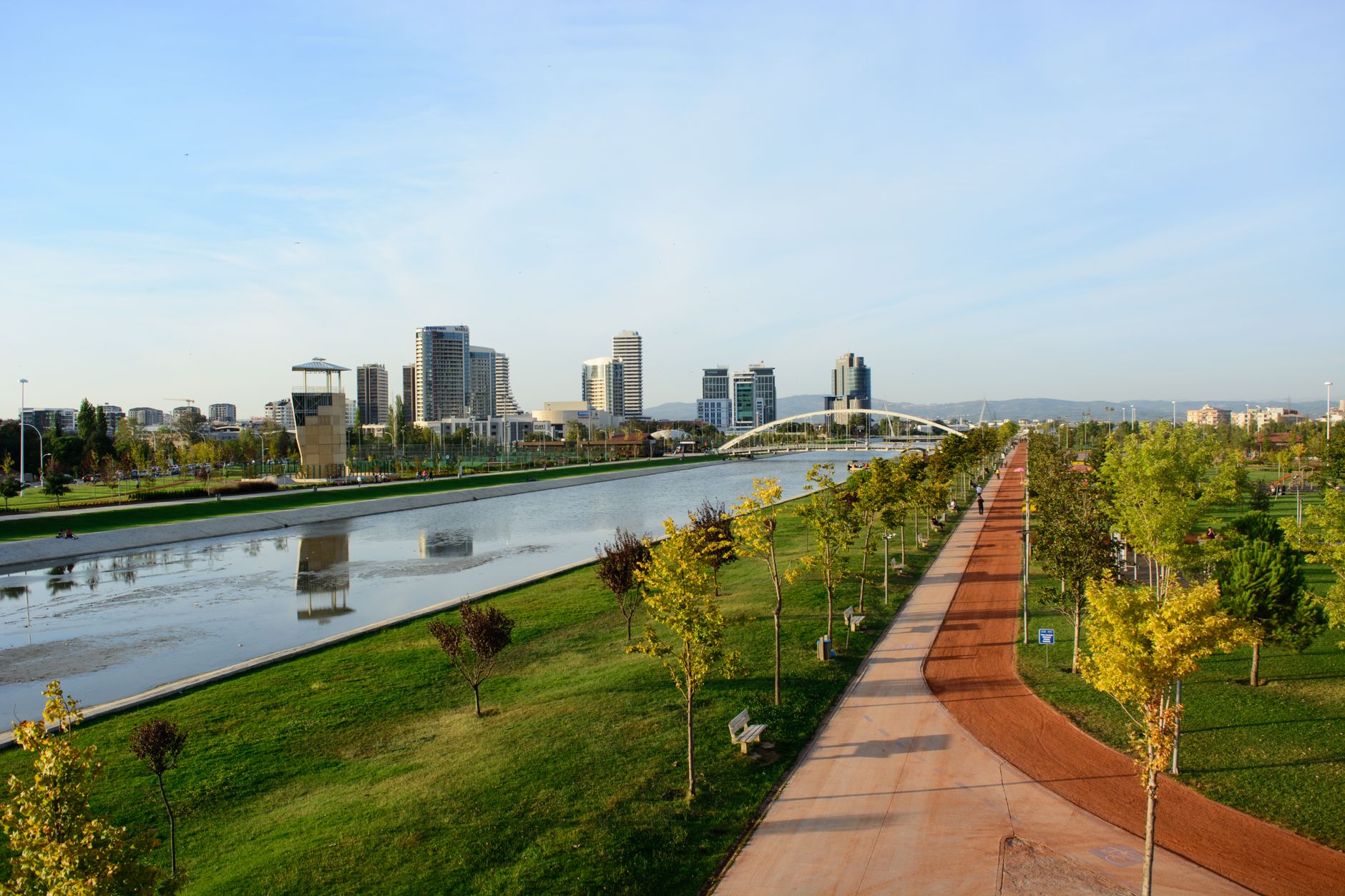 A peaceful park in Bursa featuring green landscapes, a river, and modern skyscrapers in the background.