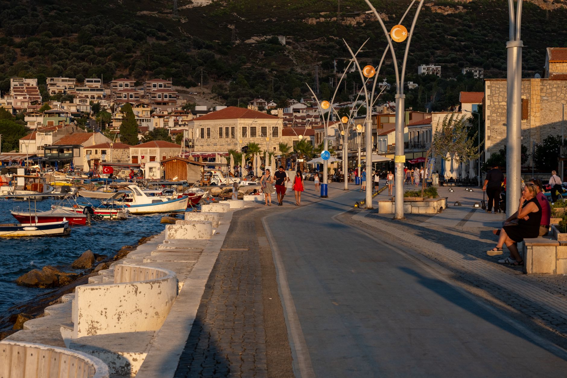A serene coastal promenade in Izmir, with boats moored and sunset light casting shadows, ideal for leisurely walks.