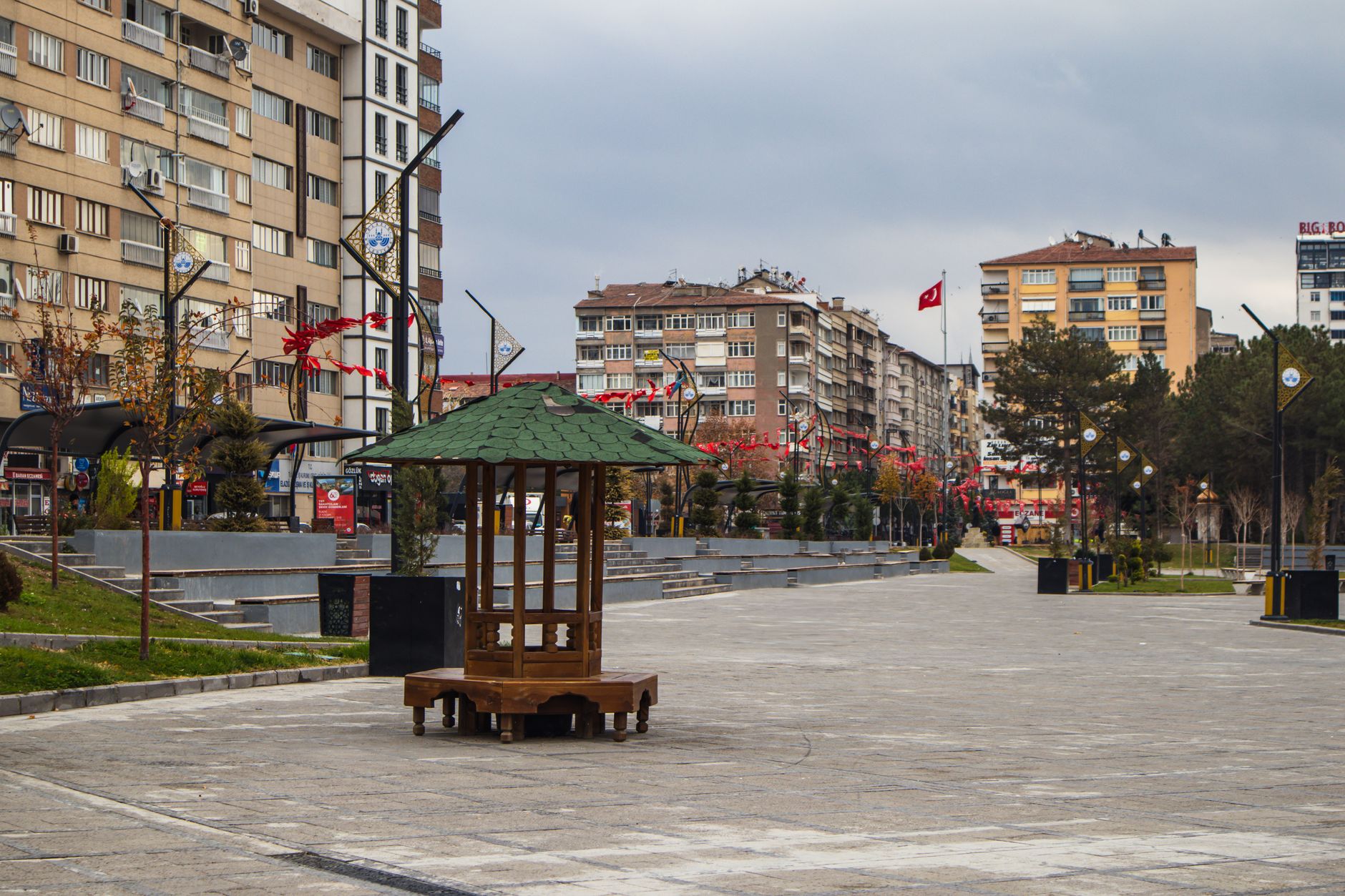 Serene square in Kayseri with a wooden gazebo, trees, and urban buildings.