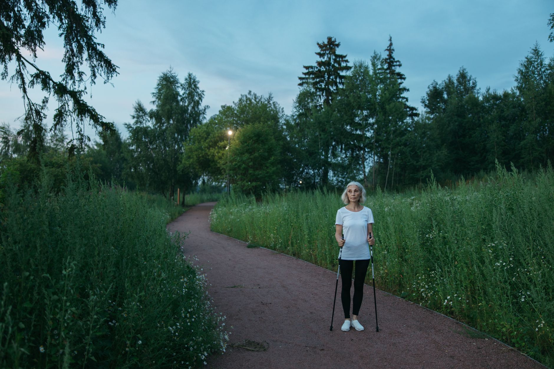 An older woman walks gently on a path surrounded by greenery in Mersin.