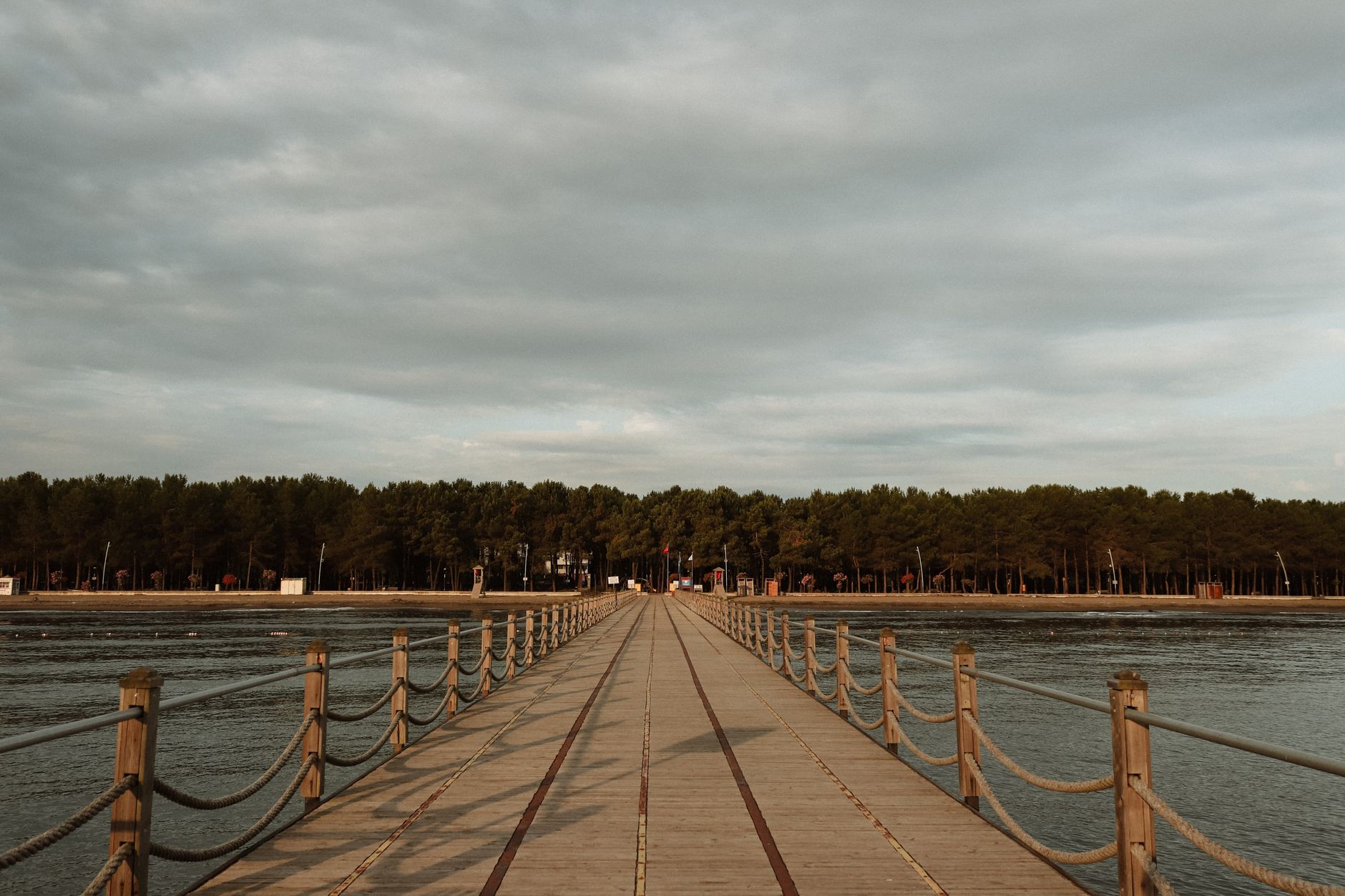 A long wooden pier stretches over calm waters, surrounded by lush greenery in a park in Samsun.