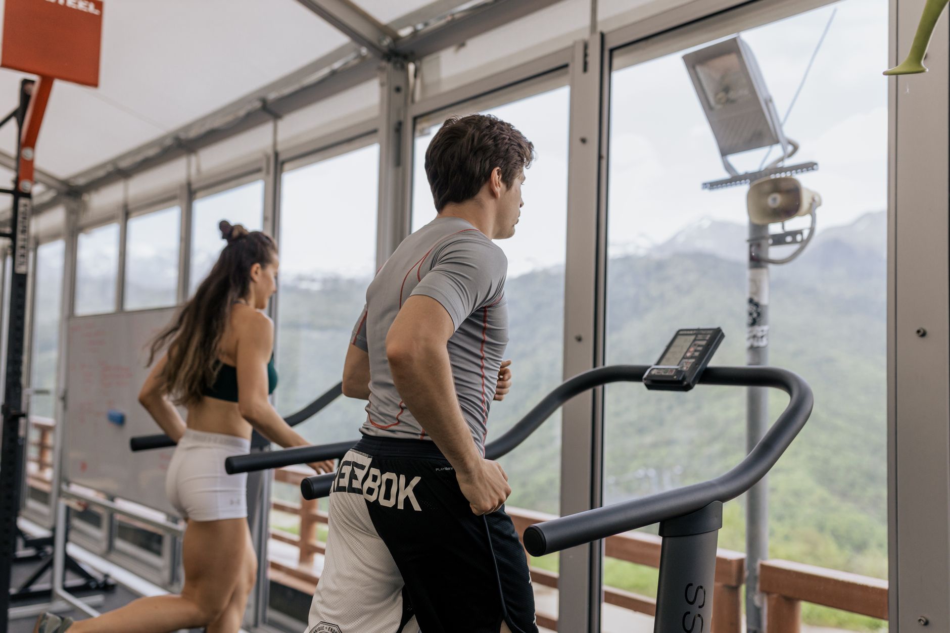 An athlete runs on a treadmill in a cardiology clinic with scenic mountain views.