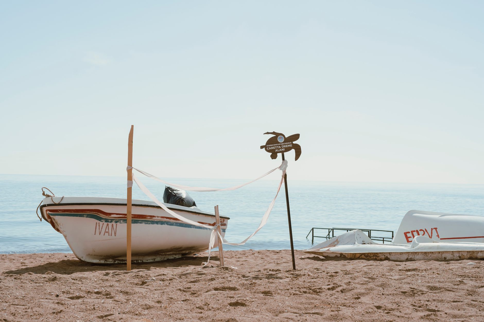 A scenic view of a sandy beach with a boat and a sea turtle nesting sign.