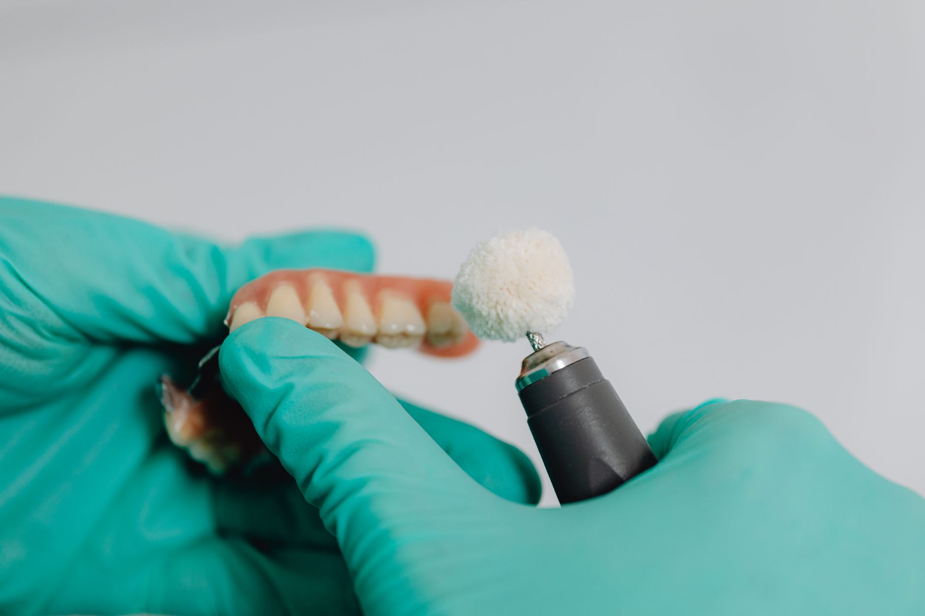 A dental technician in green gloves polishes custom provisional teeth using a dental tool.