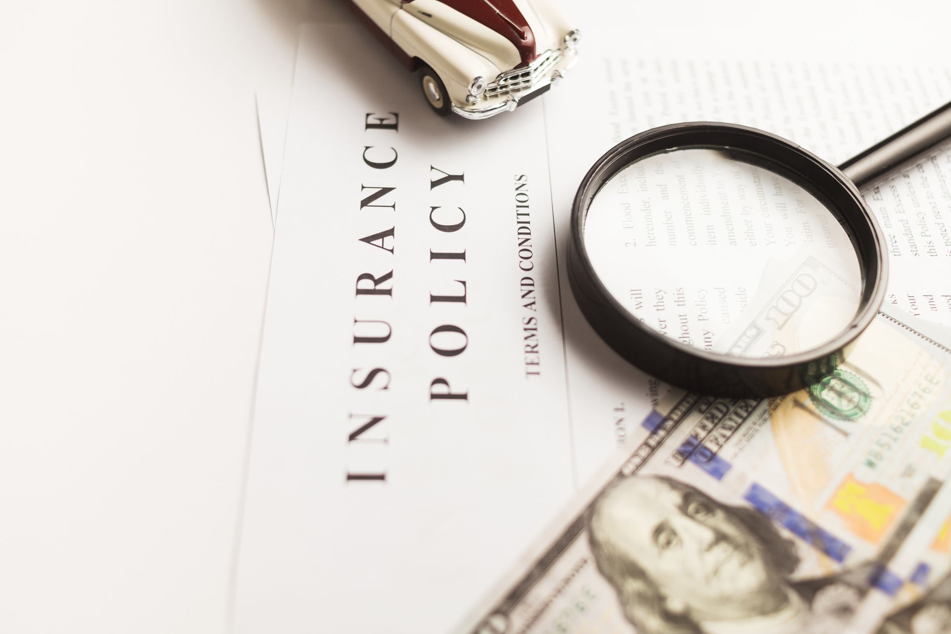 Travel insurance policy document with magnifying glass, cash, and a vintage toy car.
