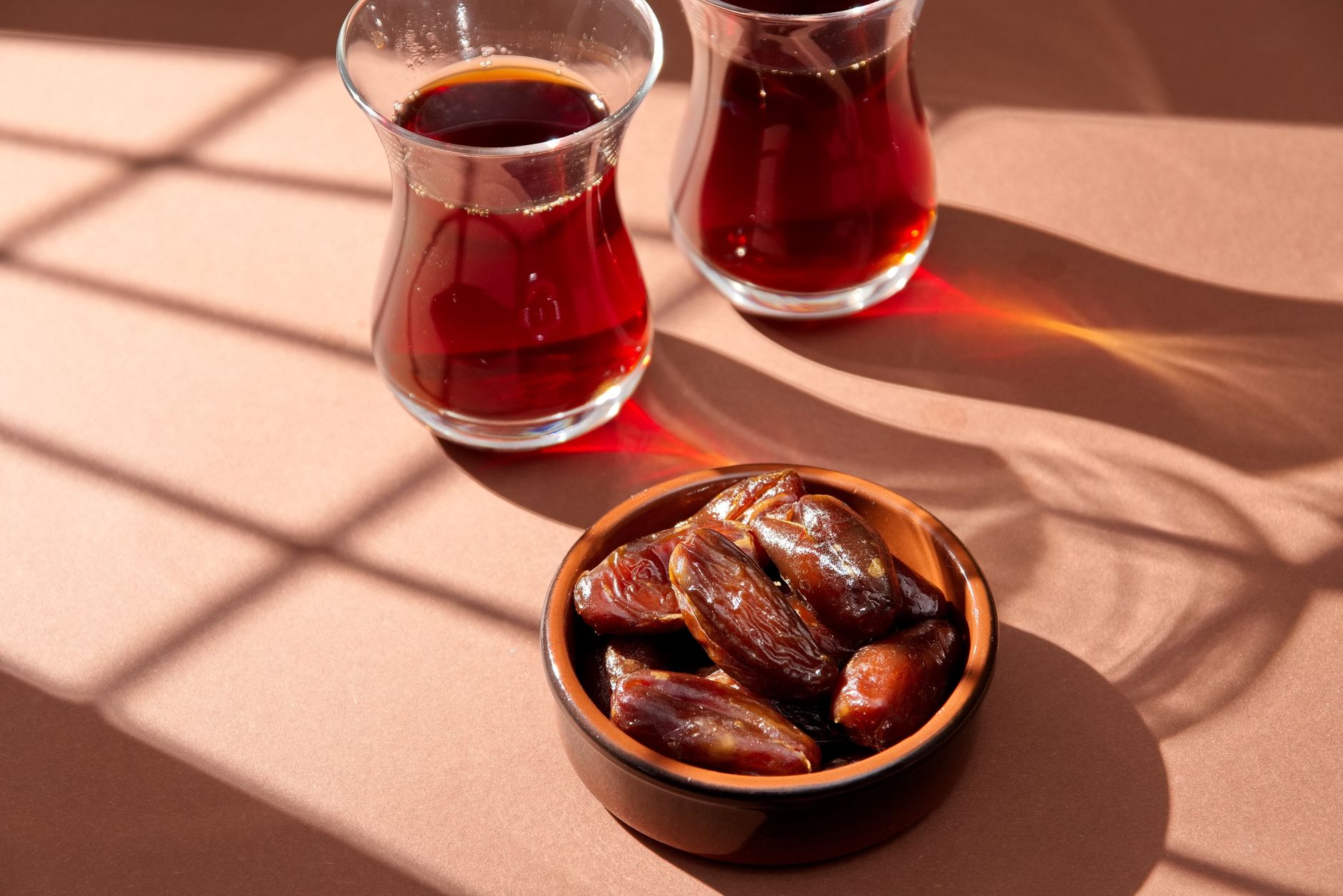 A bowl of dates next to two glasses of Turkish coffee on a brown background, highlighting a traditional iftar meal.