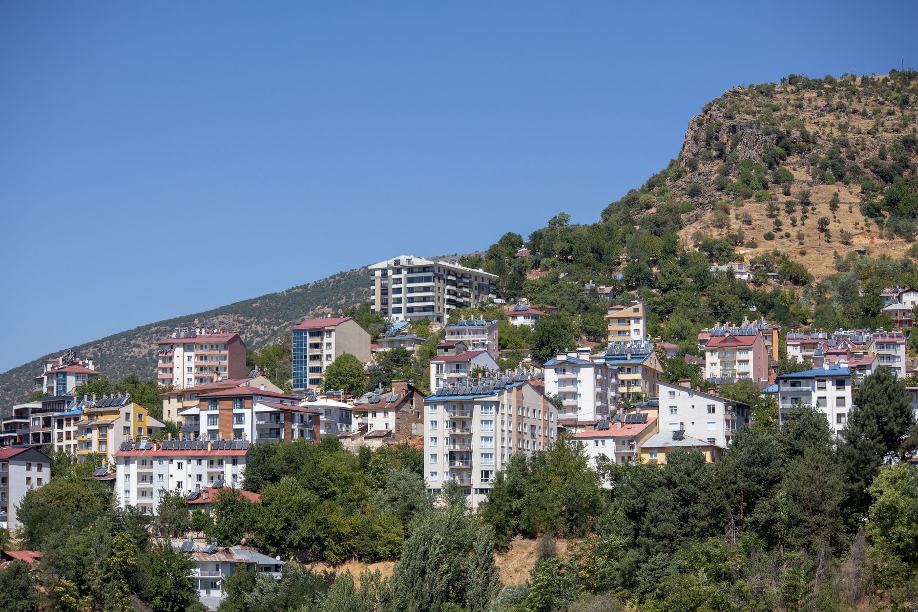 Berrak mavi gökyüzü altında yeşilliklerle çevrili çeşitli evlerin bulunduğu bir yamaç yerleşim alanı.