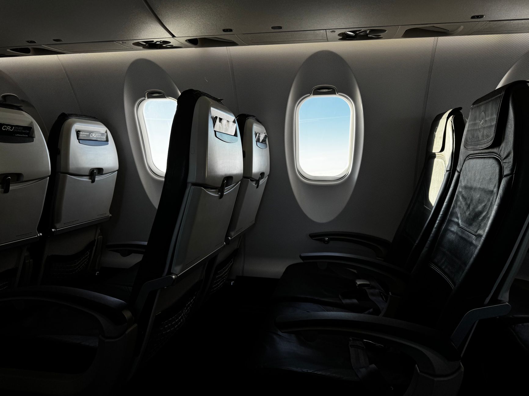 Interior view of an aircraft cabin showing empty seats and a scenic sky through the window.