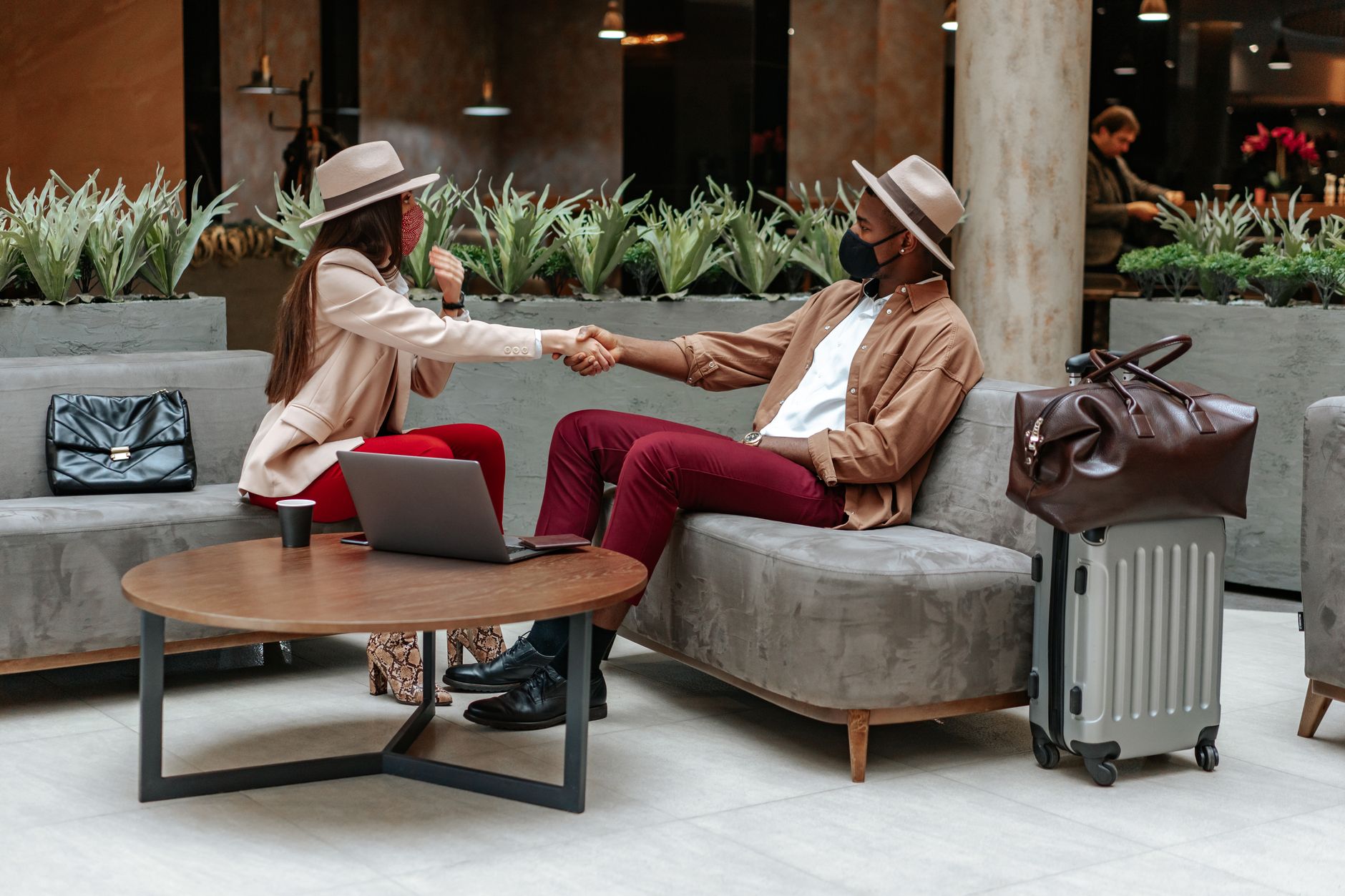 Two individuals in stylish attire shake hands in an airport lounge.
