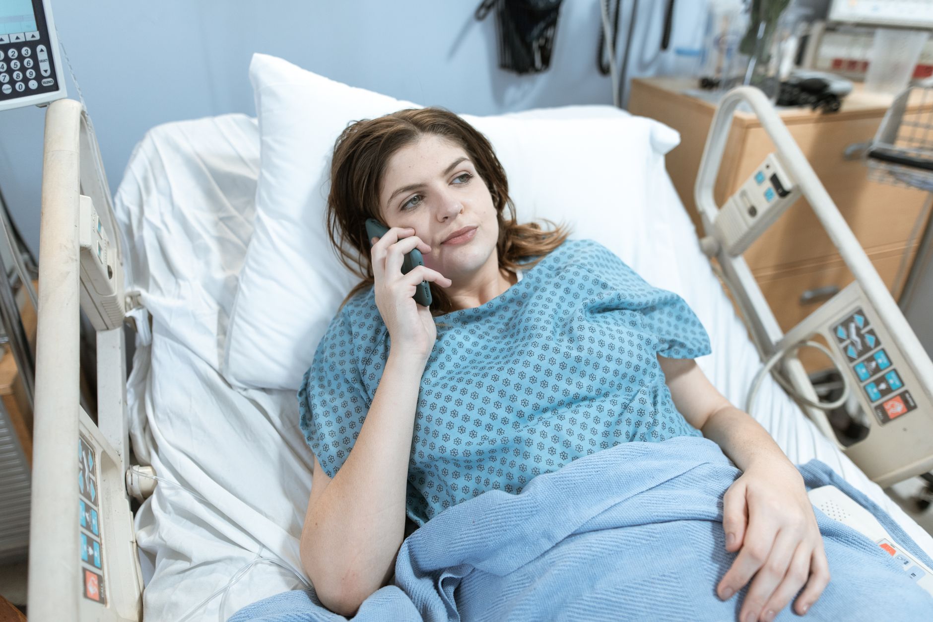A woman in a hospital bed wearing a gown speaks on the phone, showcasing a supportive environment.