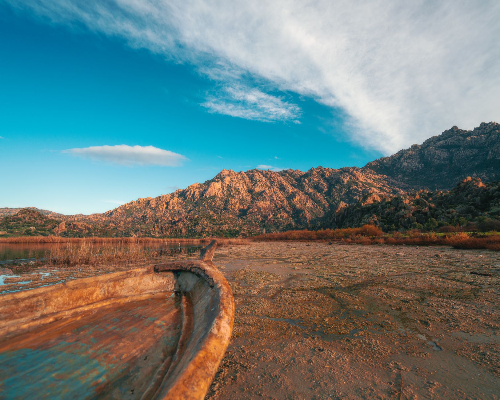 An old wooden boat rests on dry land by Lake Bafa, surrounded by mountains.
