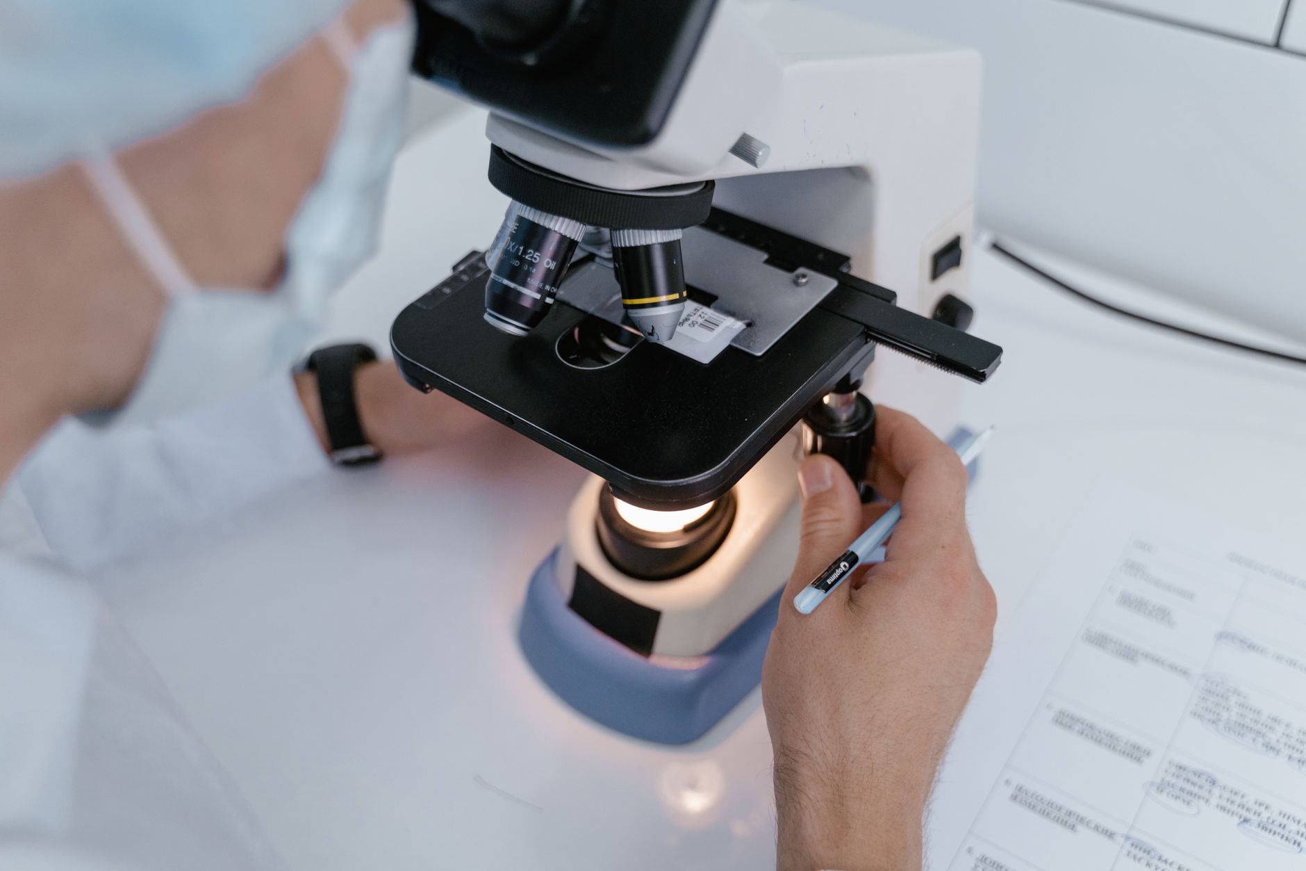 A medical professional examining a sample under a microscope in a lab setting.