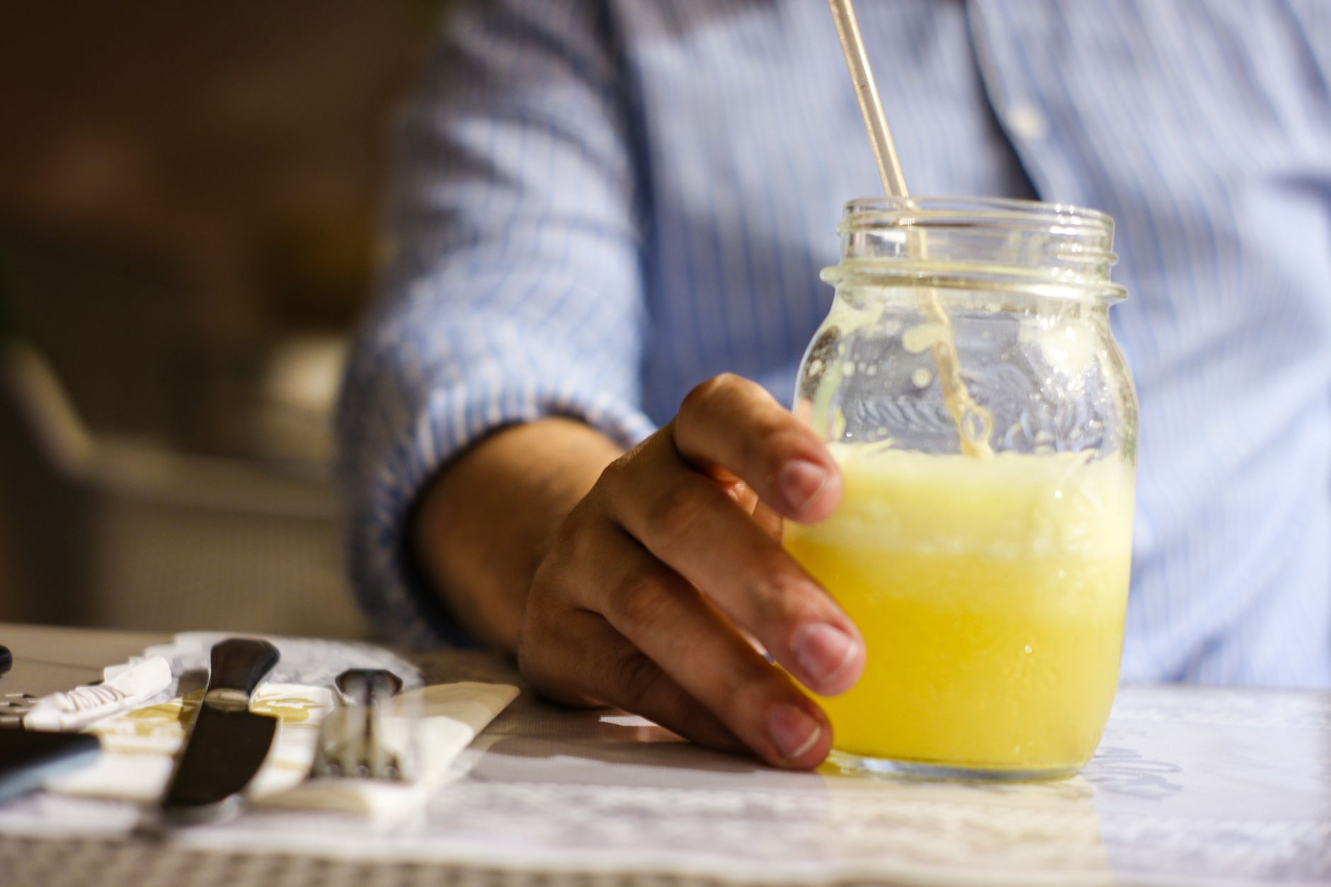 A hand holding a glass jar of limonata with lemon slices, set on a café table.