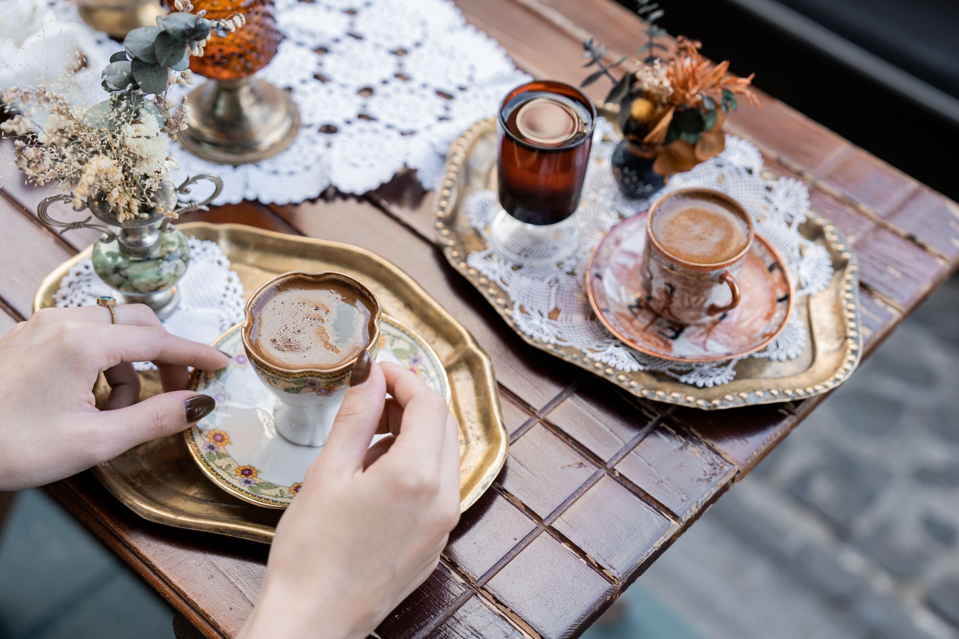 A hand holding a beautifully crafted coffee cup on a golden tray, adorned with lace.
