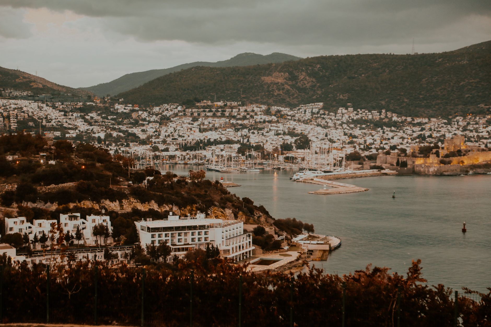 Scenic view of Bodrum harbor featuring a ferry, the iconic Bodrum Castle, and surrounding coastal town.
