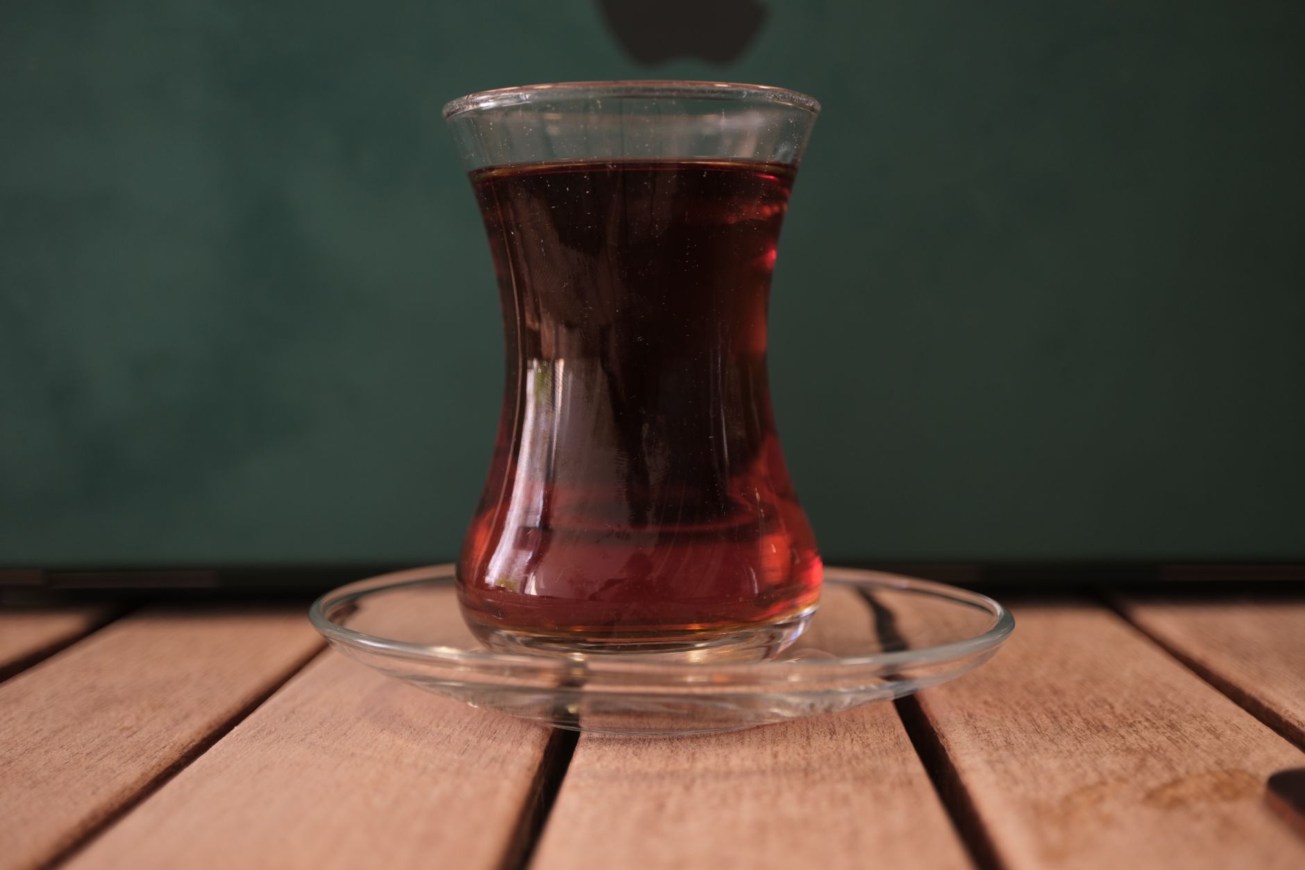 A tulip-shaped glass of Turkish tea on a glass plate, set on wooden deck.
