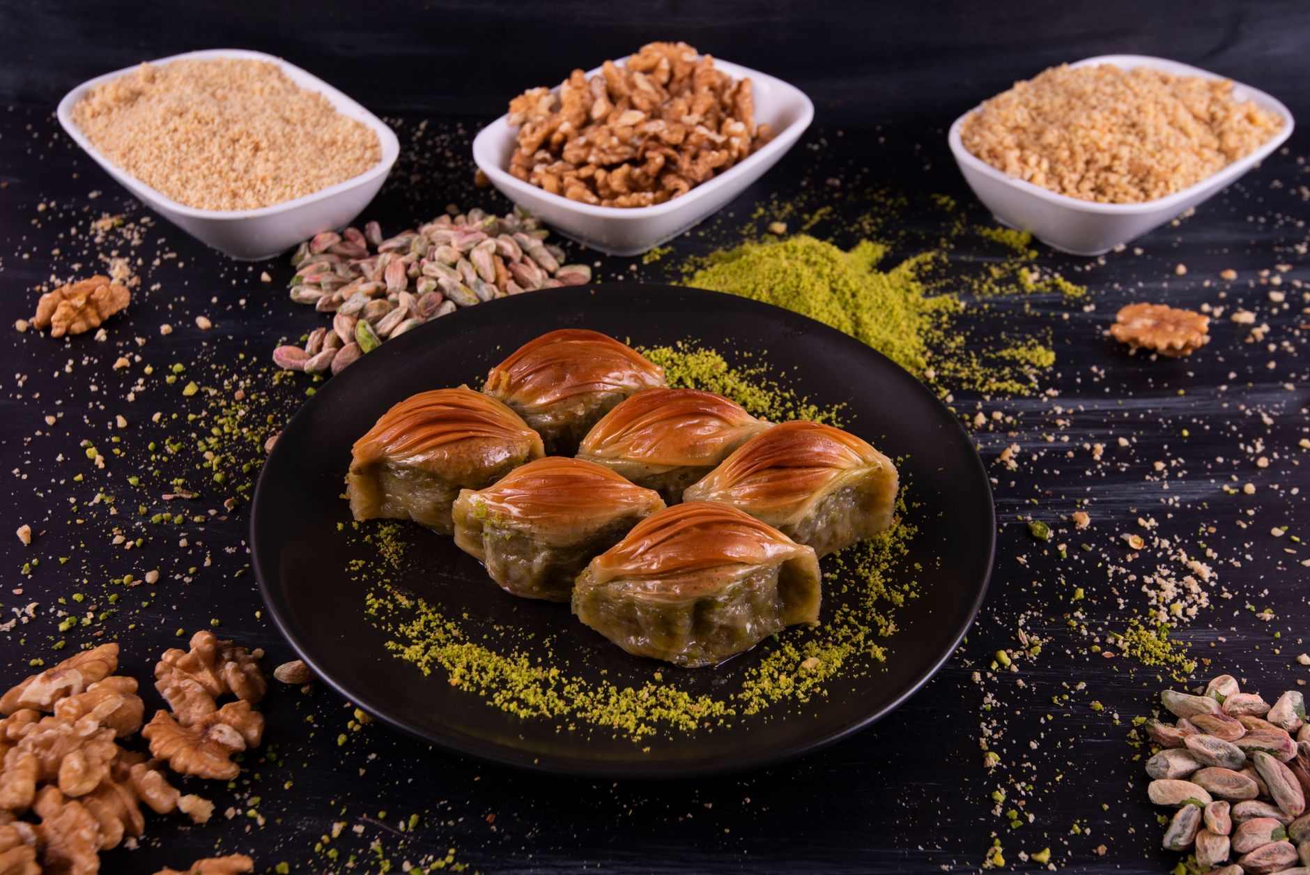 Kıyılmış kuruyemiş ve baharatlarla çevrili, güzelce düzenlenmiş bir baklava tabağı.