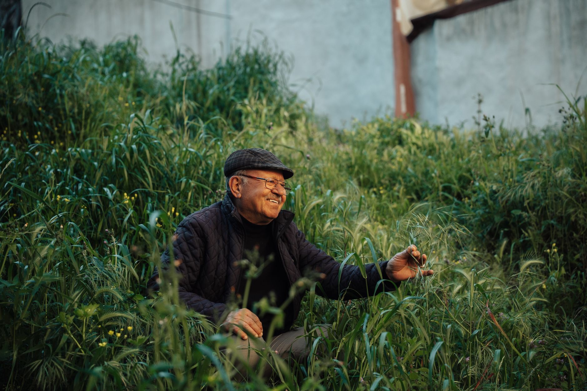 Smiling elderly man sitting in tall grass, reflecting joy and comfort in nature.