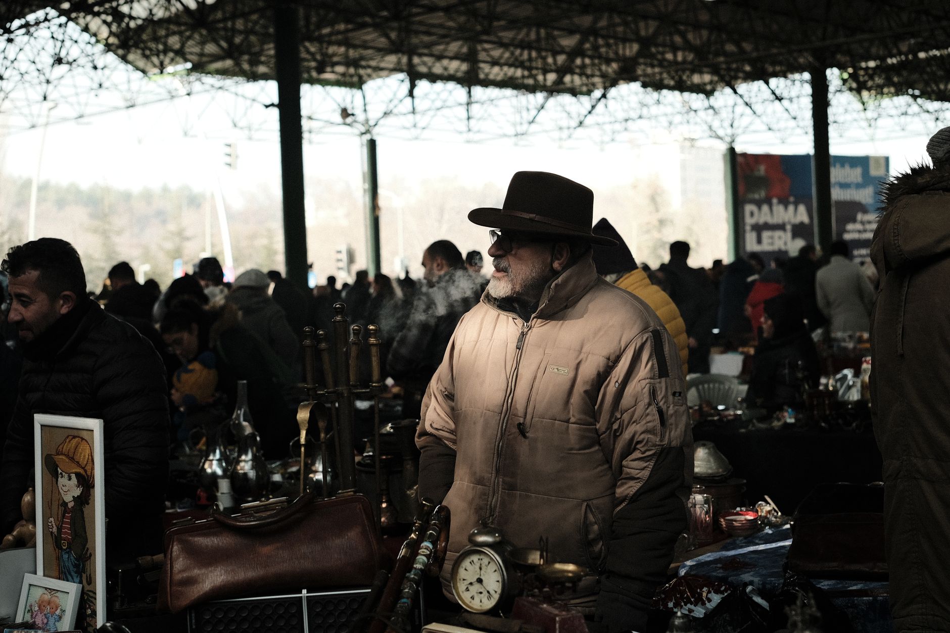 مردی با کت قهوه‌ای در یک بازار قدیمی شلوغ، احاطه‌شده با عتیقه‌جات.