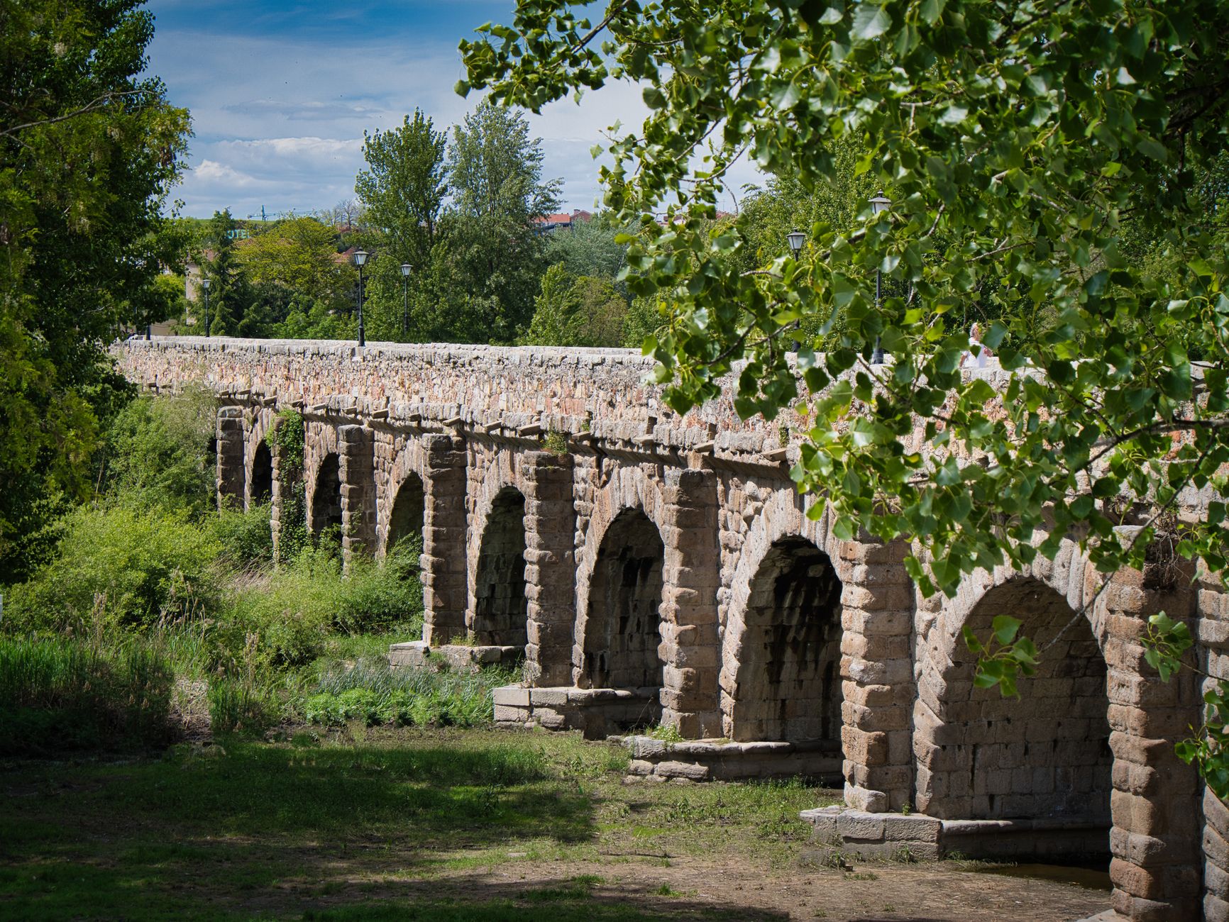 Detailed view of an ancient stone bridge with arches, showcasing craftsmanship amidst lush greenery.