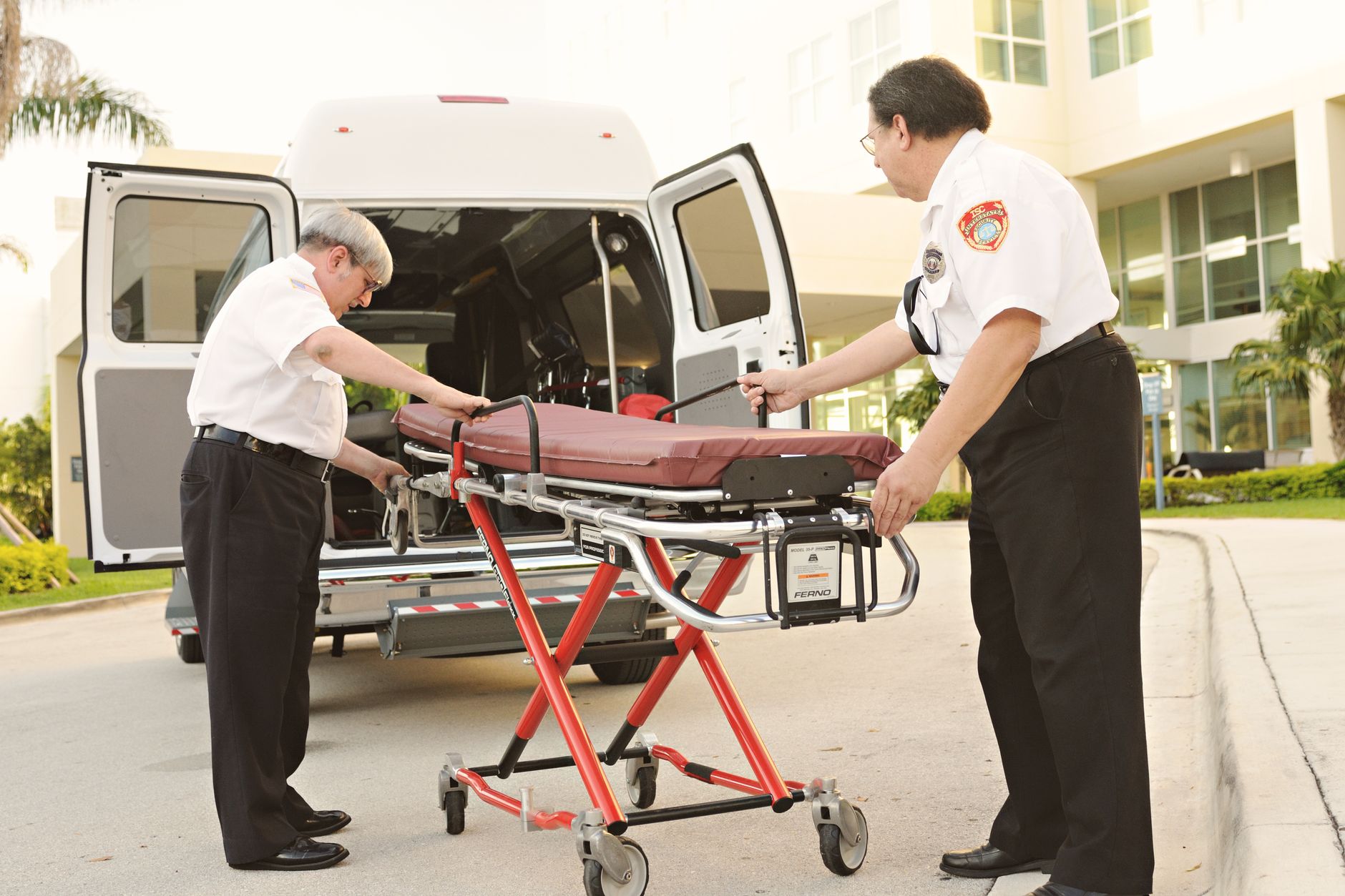 Two paramedics using a stretcher to transfer a patient from an ambulance at an airport clinic.