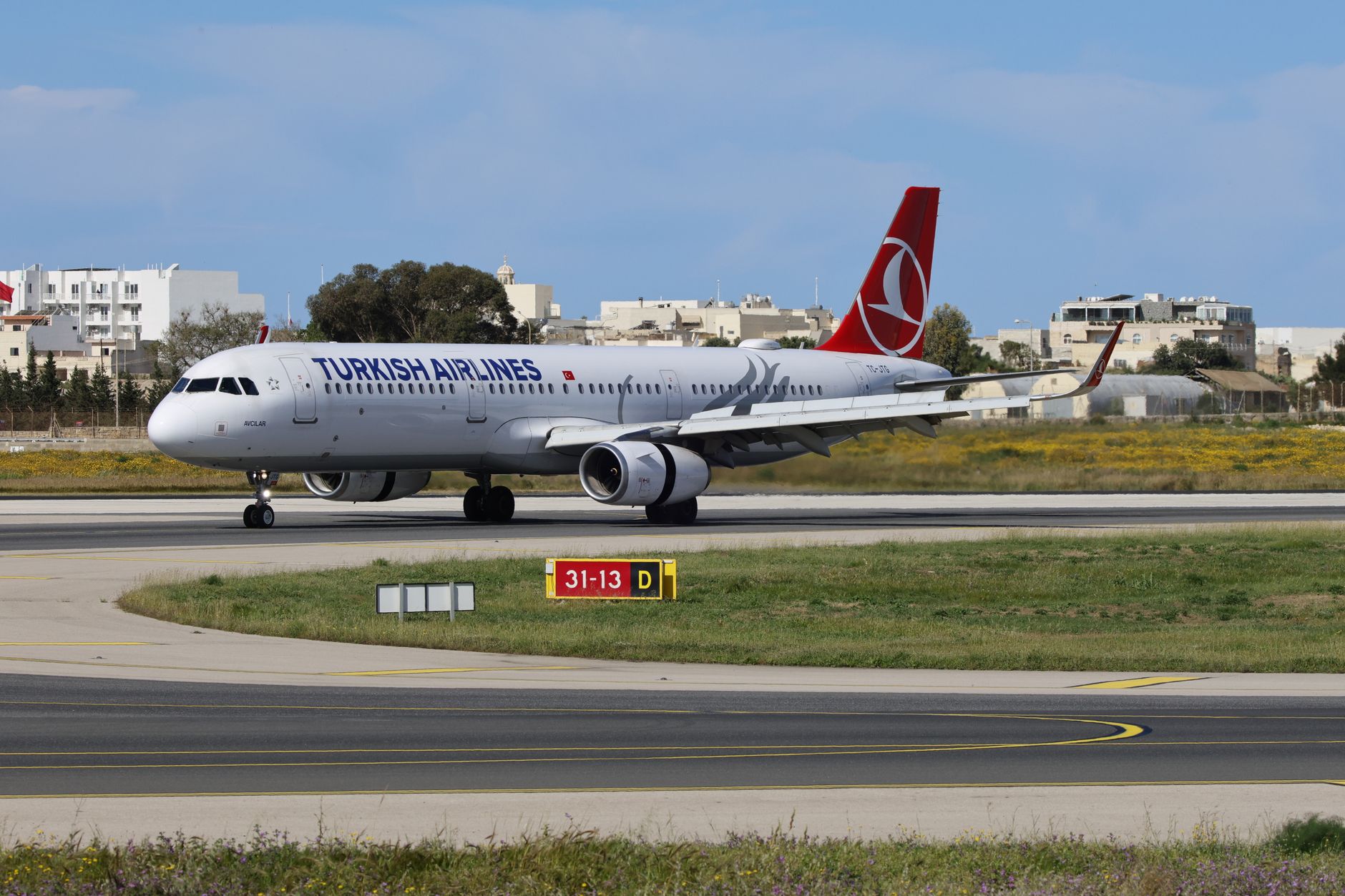 Turkish Airlines airplane taxiing at the airport under blue skies.
