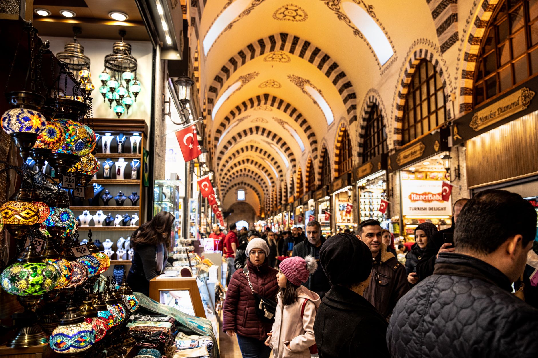 Visitors explore the bustling Grand Bazaar in Istanbul, filled with colorful lamps and local goods.