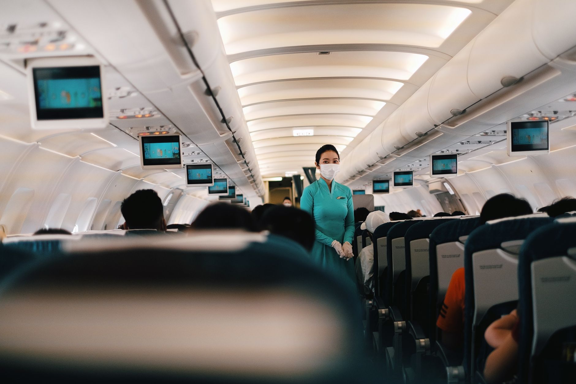 Cabin crew in turquoise uniform assisting passengers in an airplane.
