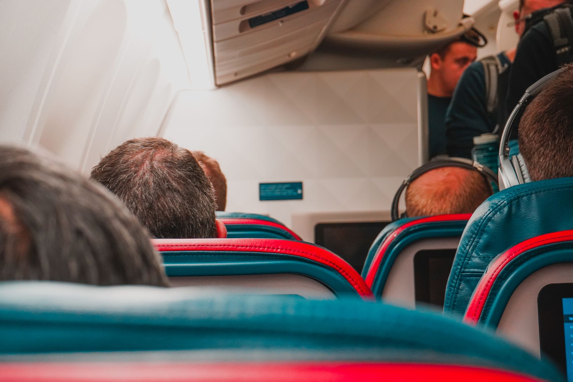 Back view of passengers in a plane, showcasing a comfortable in-flight experience with headphones and colorful seats.