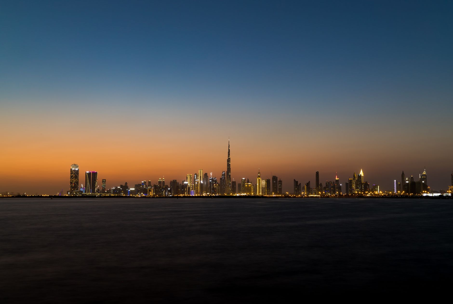 A panoramic view of Dubai's skyline at sunset, showcasing tall buildings and the shimmering Gulf waters.