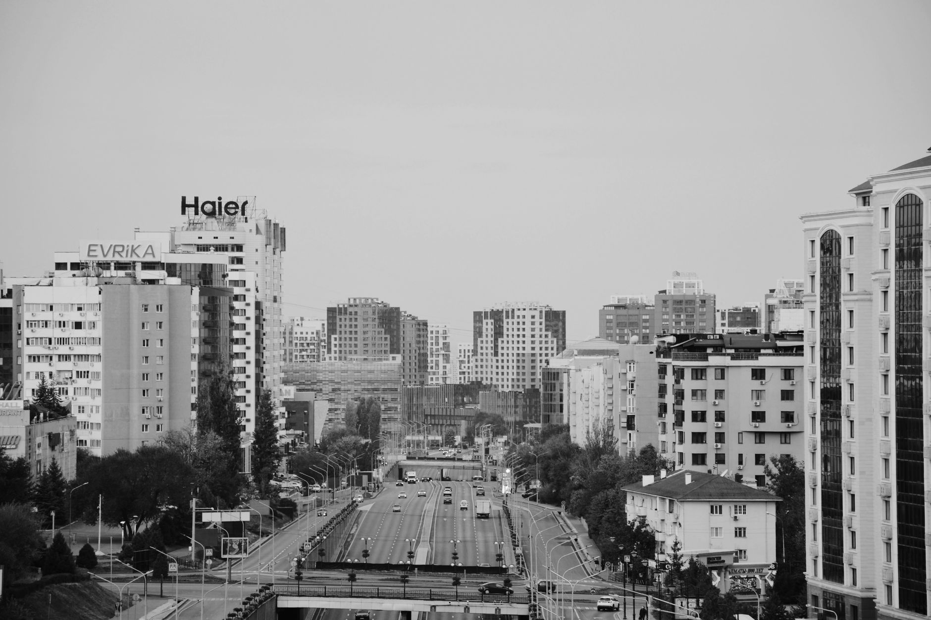 Black and white cityscape of Almaty with buildings and highways, illustrating urban life.