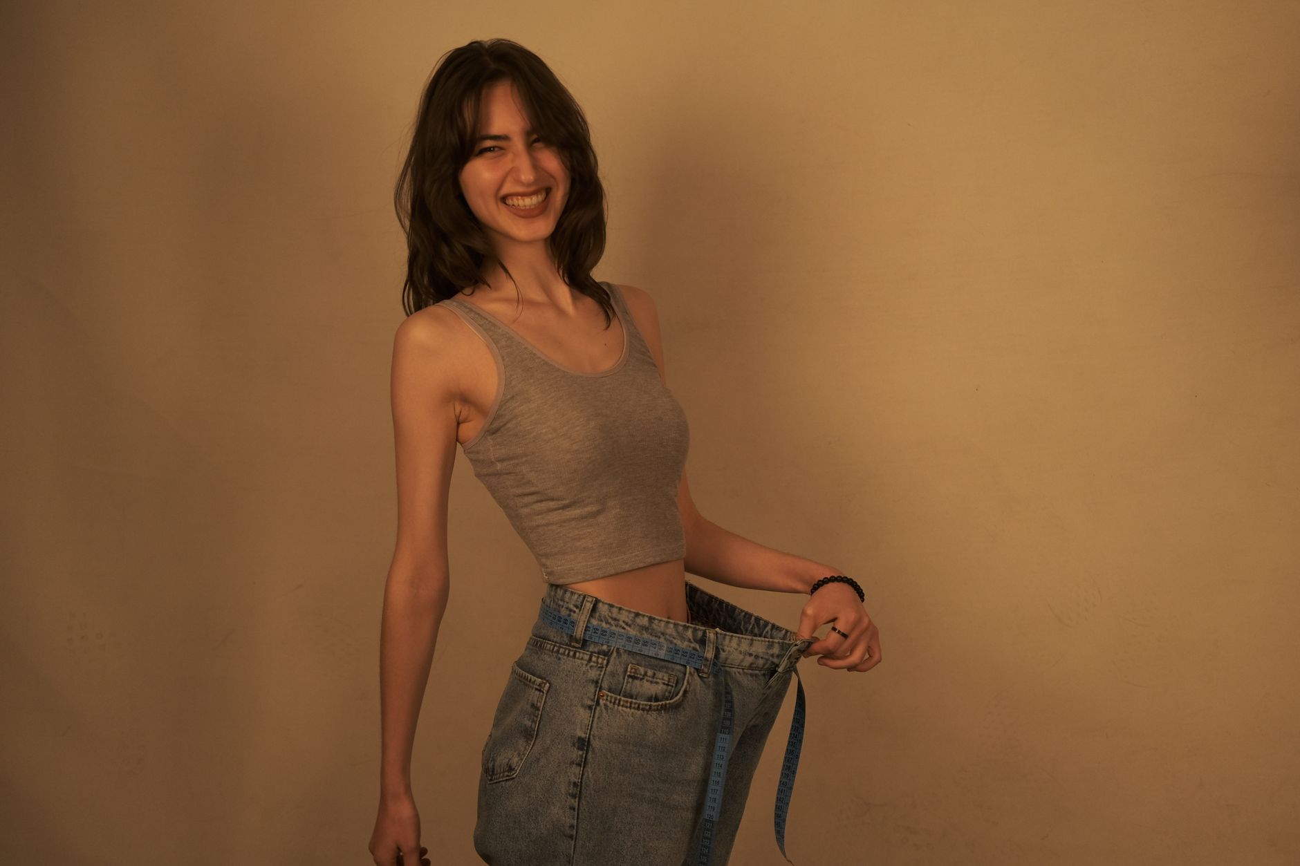 A smiling woman holding oversized jeans, celebrating weight loss success.