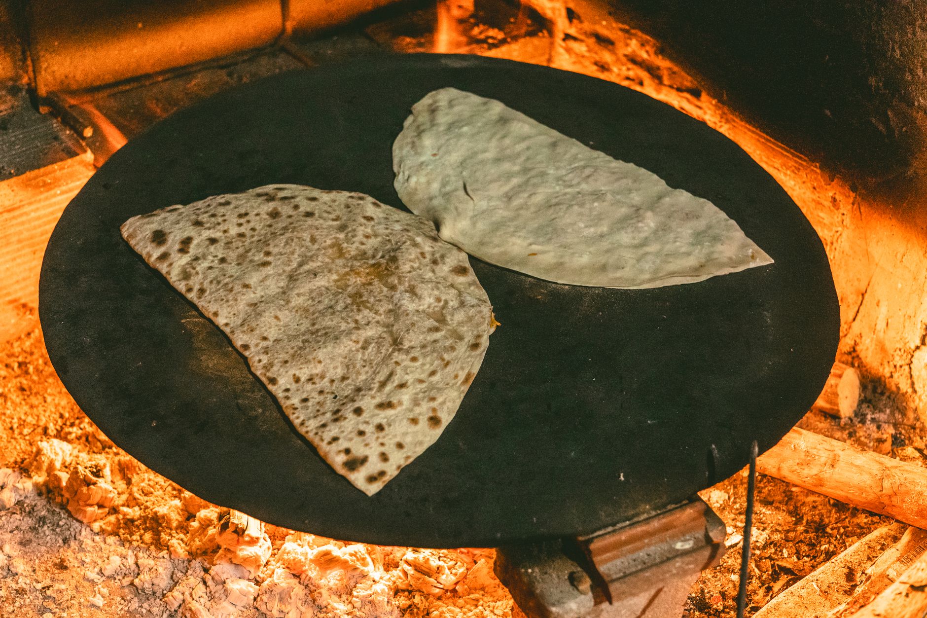 Bazlama breads cooking on a traditional sac griddle over an open flame.