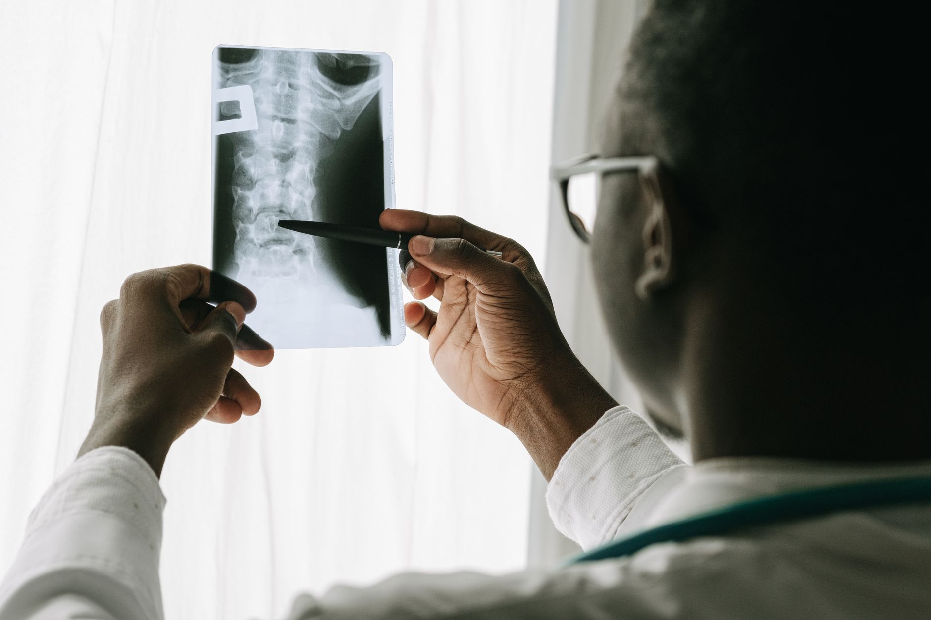 A medical professional examines an X-ray of the spine using a pen.
