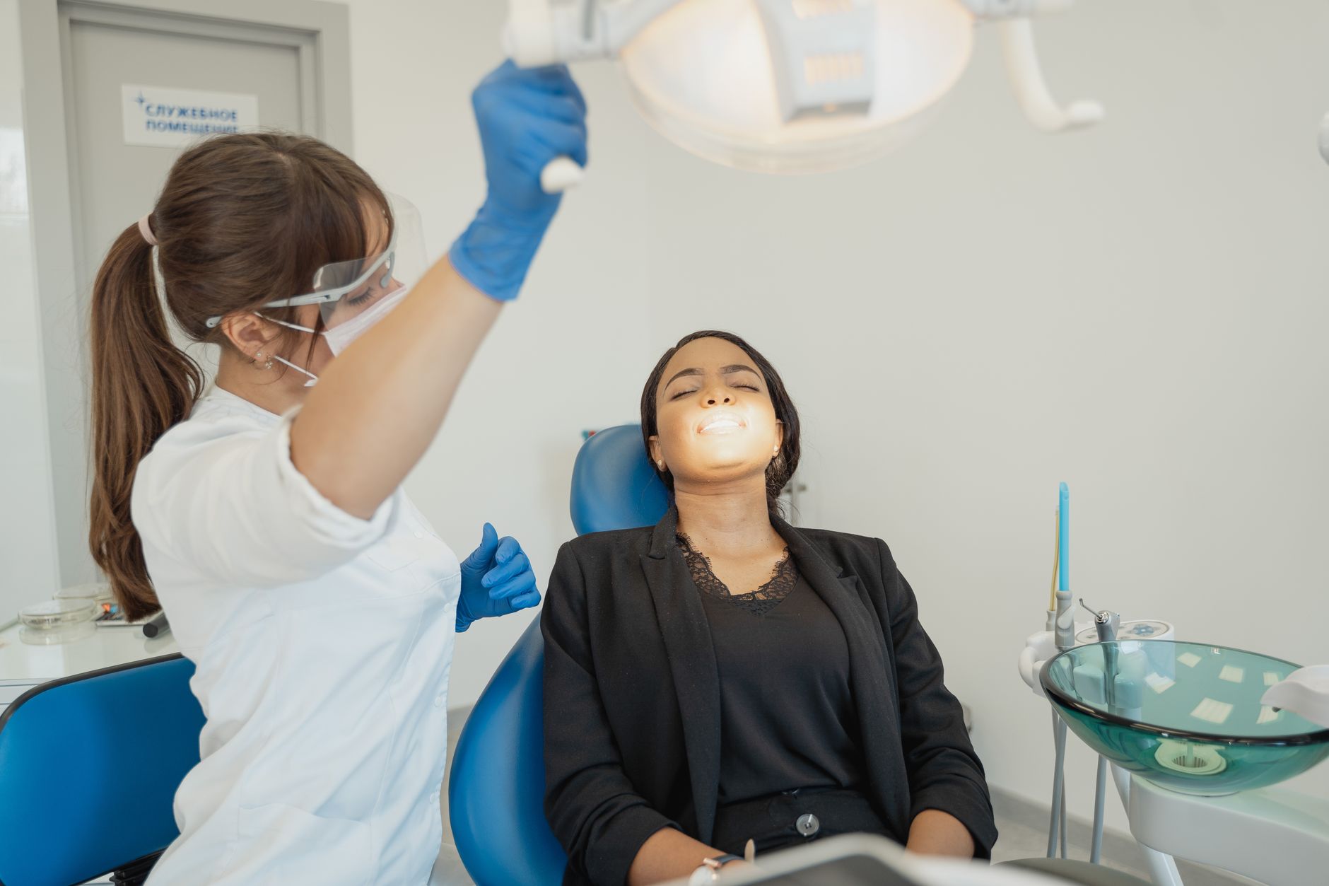 A patient smiling in a dental chair while the dentist prepares tools.