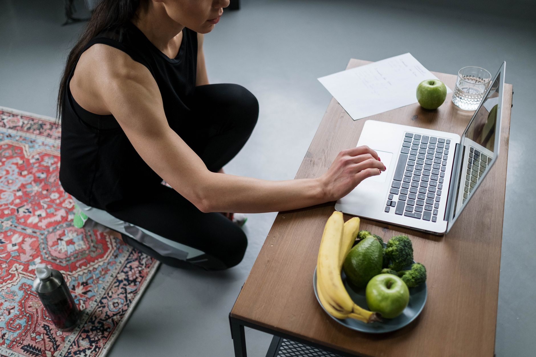 A woman working on a laptop at a wooden table with fruits and vegetables around her, promoting a balanced lifestyle.
