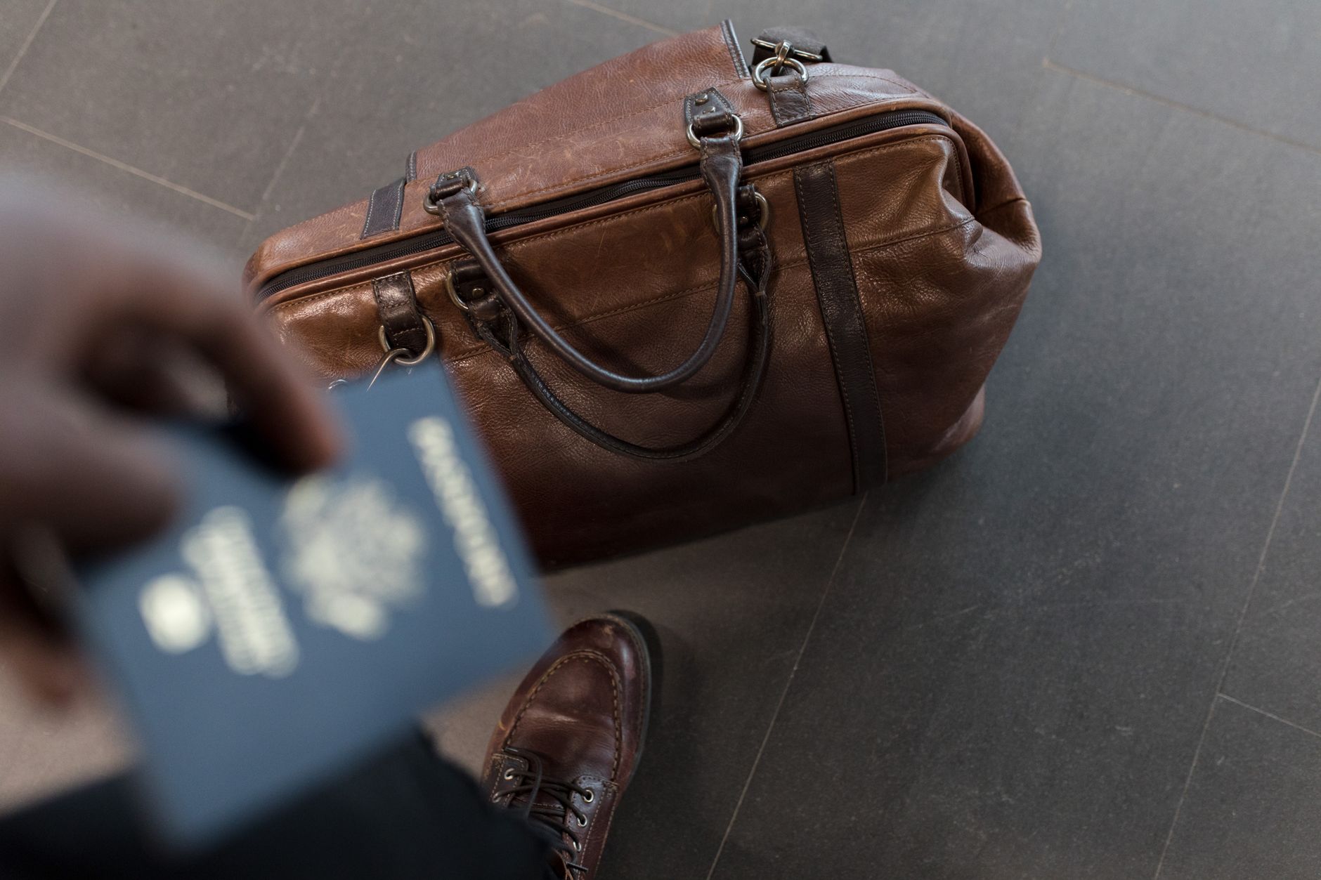 A brown leather bag and a hand holding a passport, prepared for travel.
