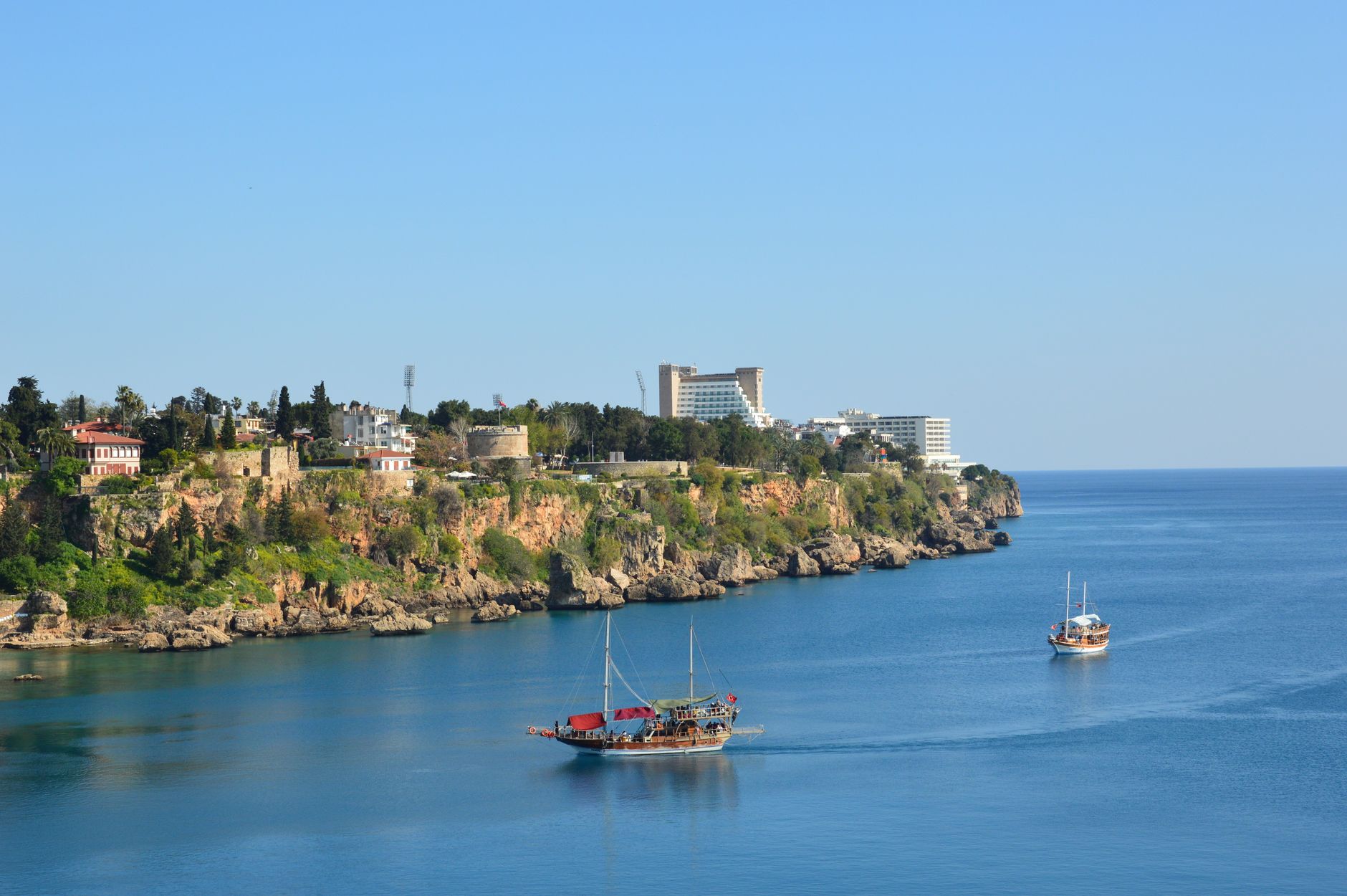 Beautiful view of Antalya's coastline featuring lush cliffs and traditional boats on calm blue waters.
