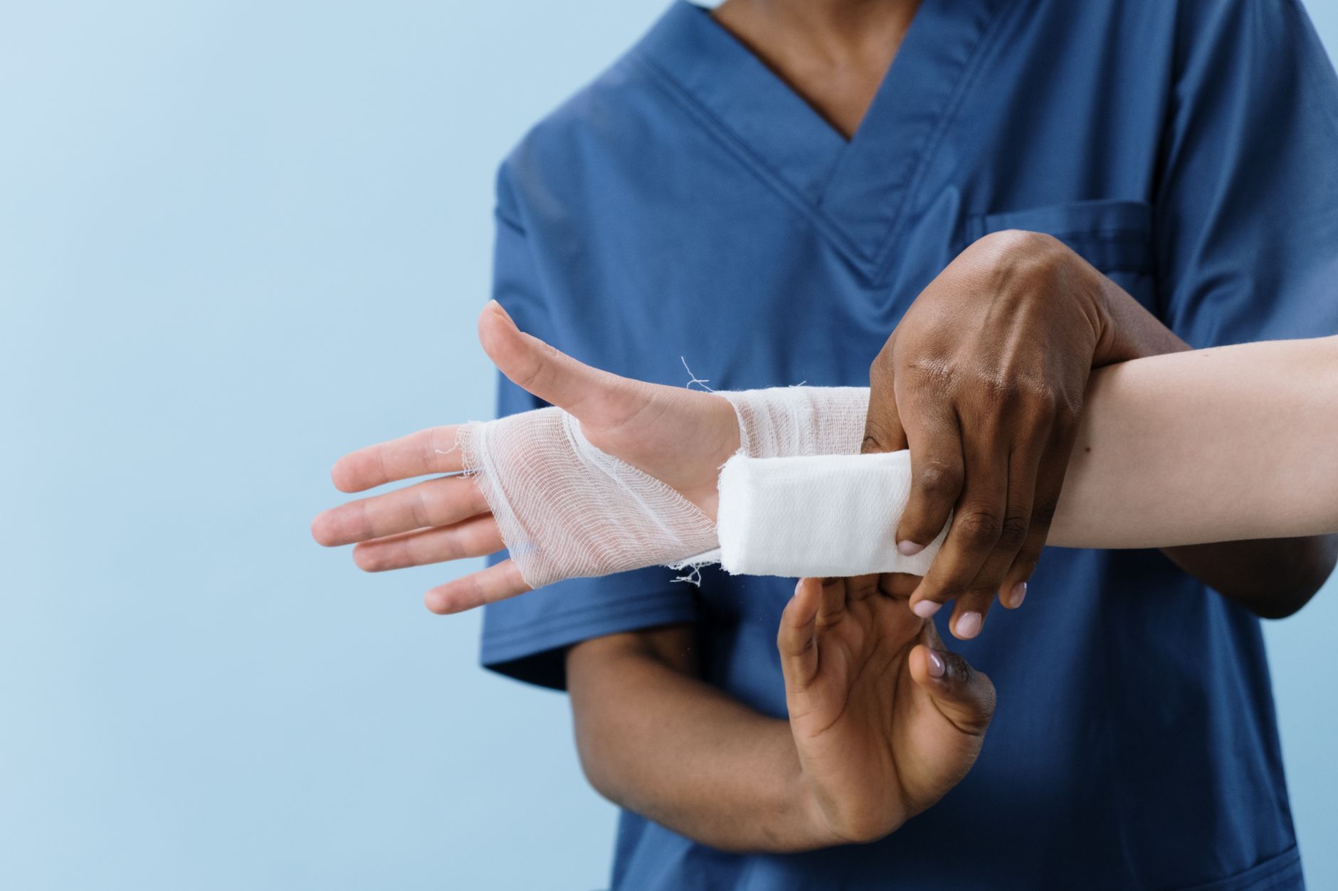A nurse wraps a bandage around a patient's injured arm in a clinic setting.