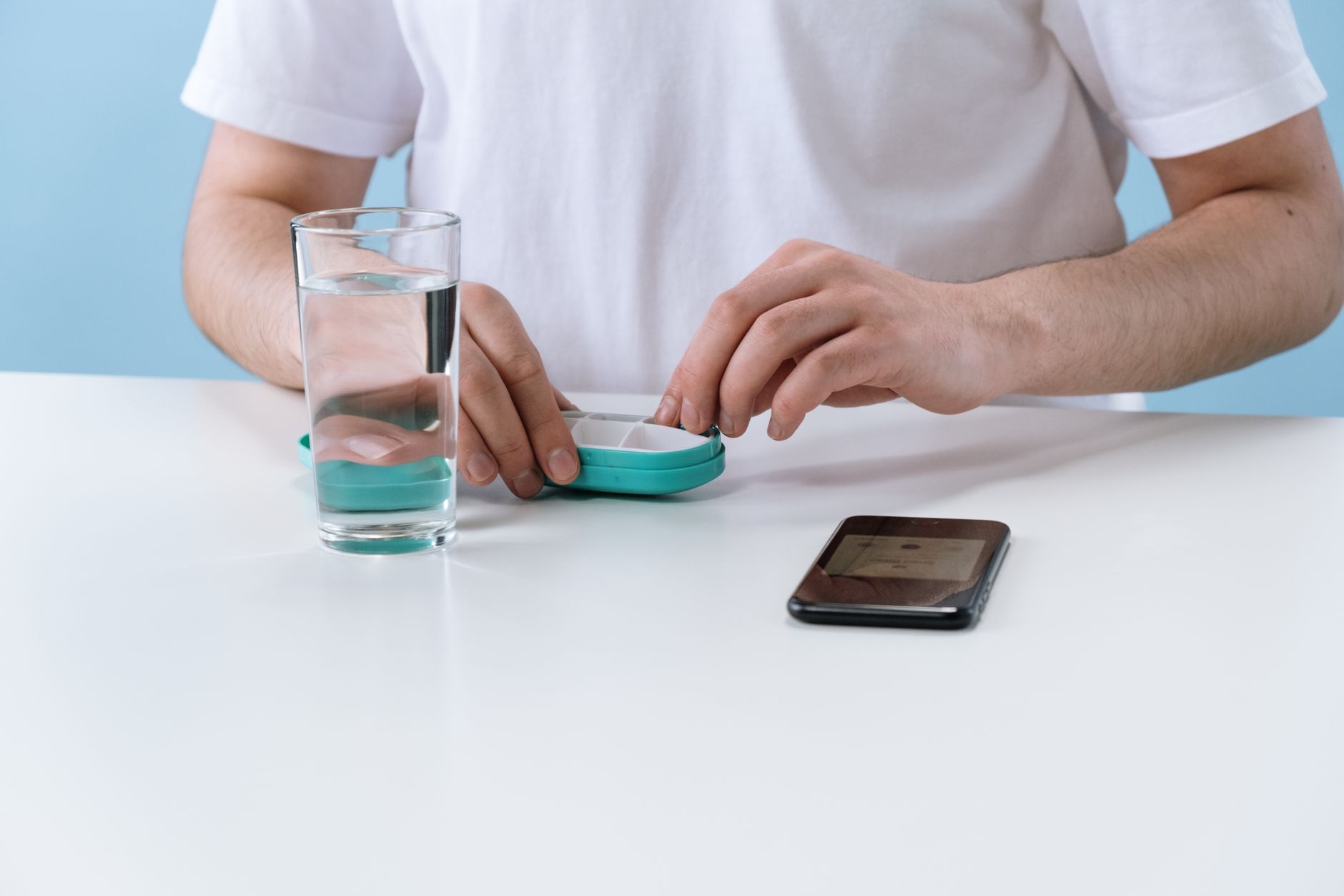 Close-up of a person organizing medication with a smartphone and glass of water.