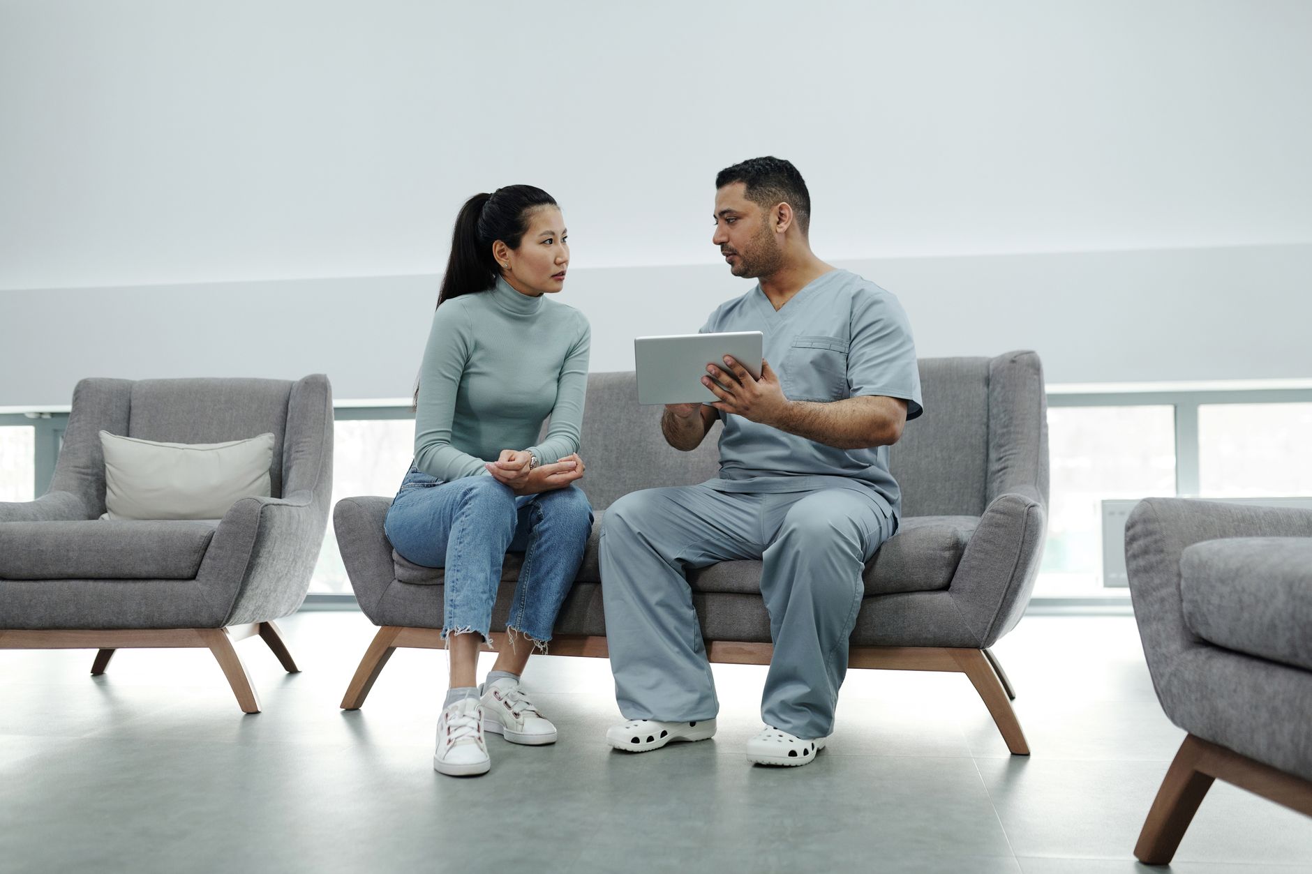 A doctor and patient discuss via a tablet in a modern clinic setting.