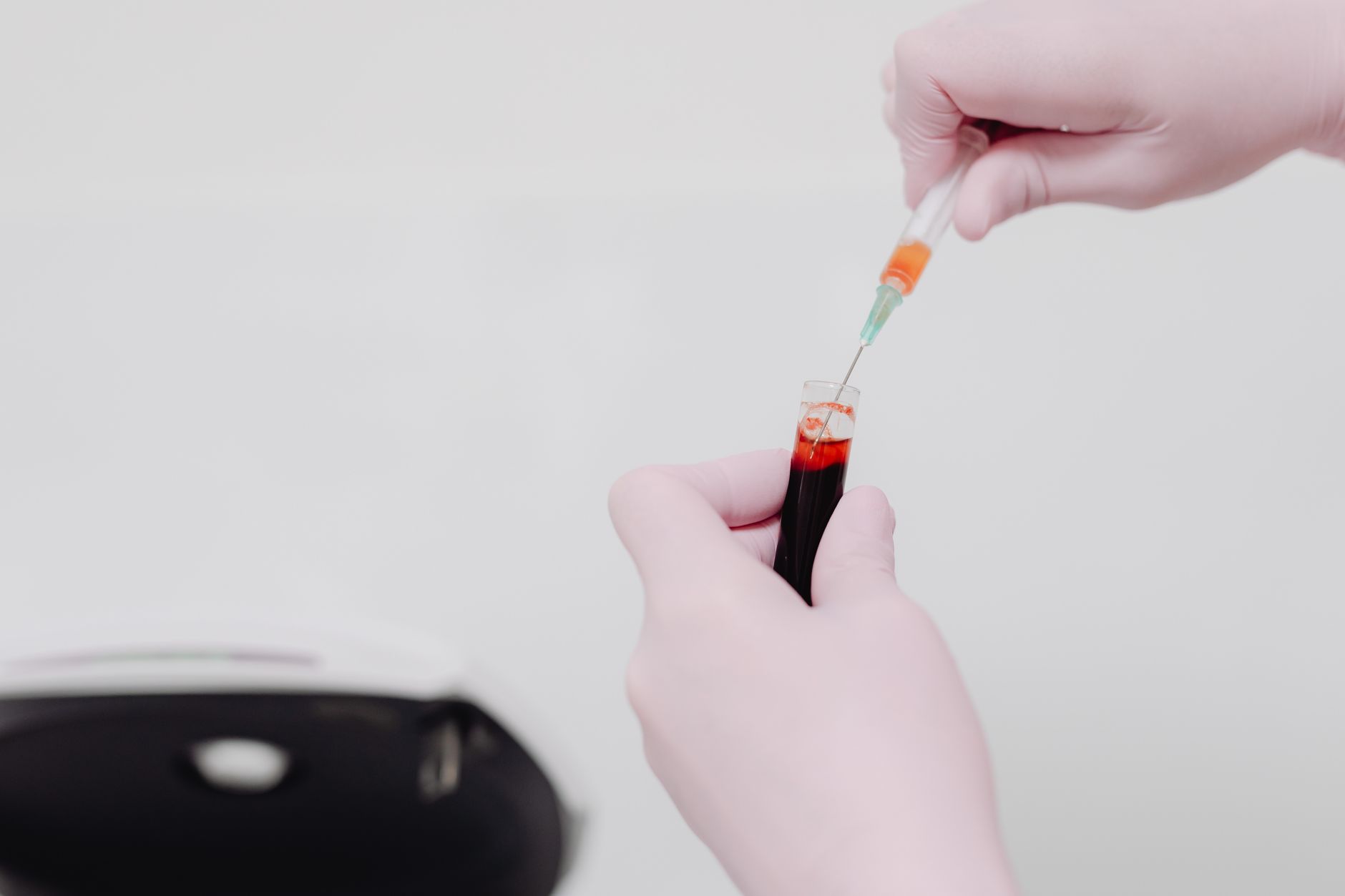 Technician in gloves using a syringe to analyze blood in a test tube.