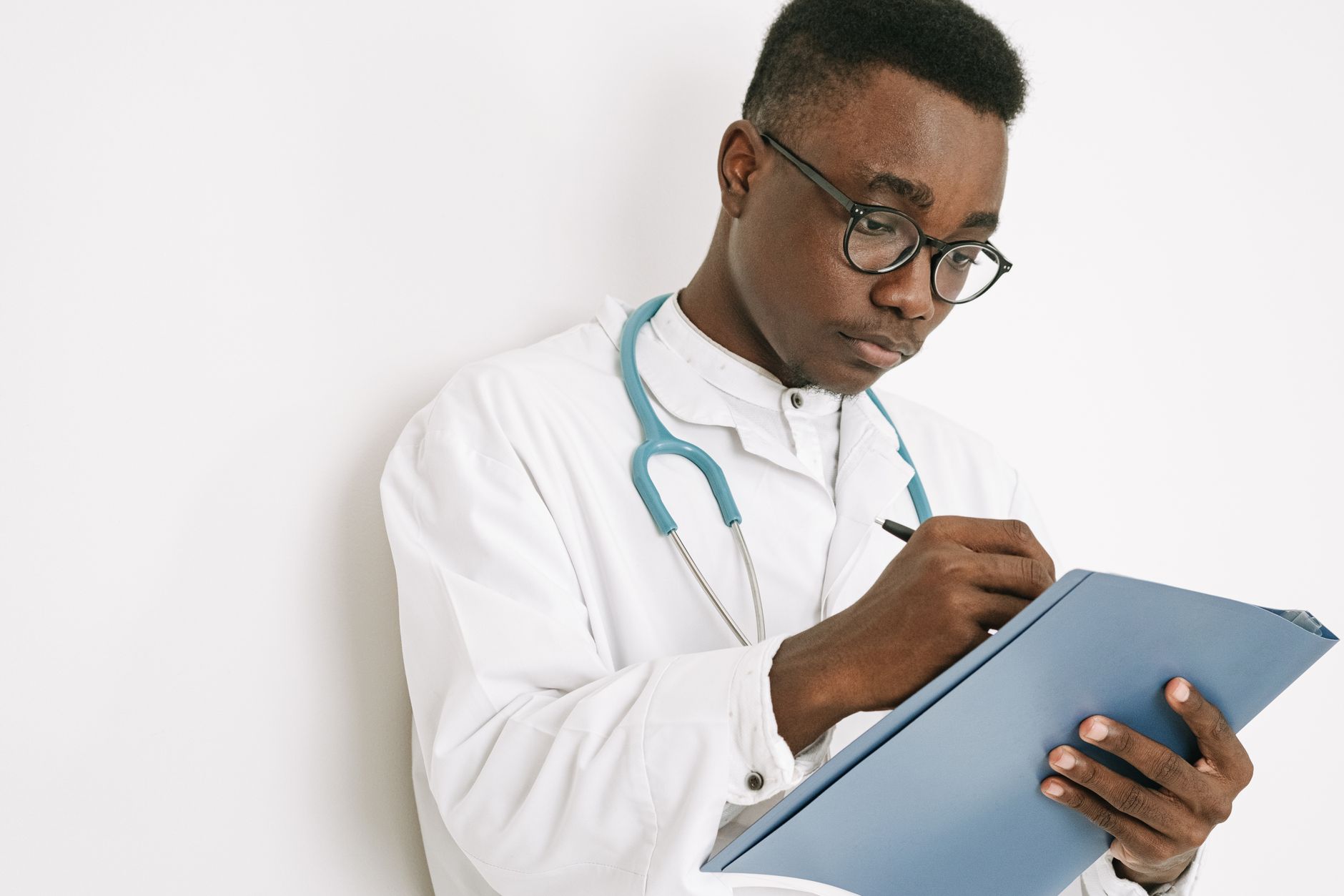 A doctor in a white coat writing notes with a stethoscope around his neck.