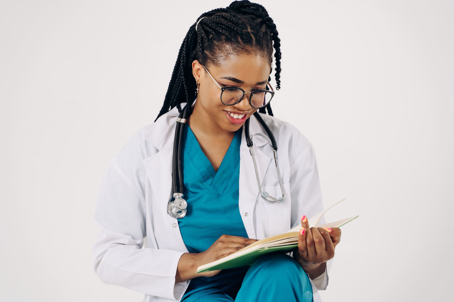 A female doctor in scrubs and a lab coat smiles while reading an aftercare guide.