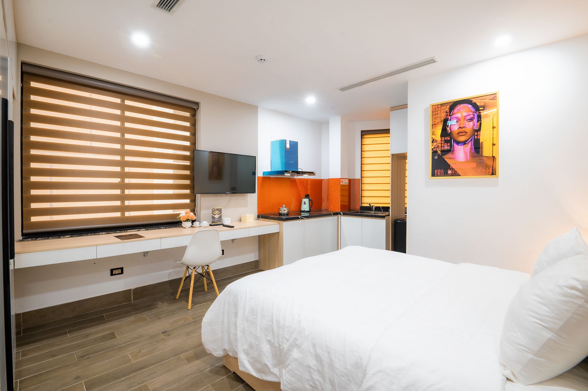 Interior of a clean, modern guest room featuring a kitchenette, bed, and workspace.