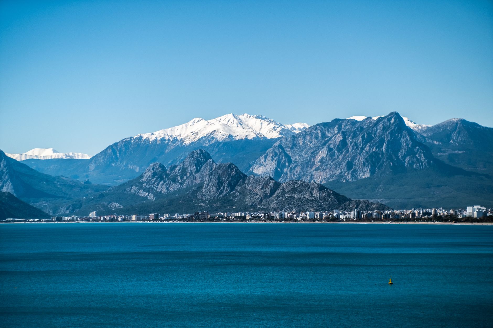A clear winter day at Antalya, showcasing snow-capped mountains and a tranquil sea.