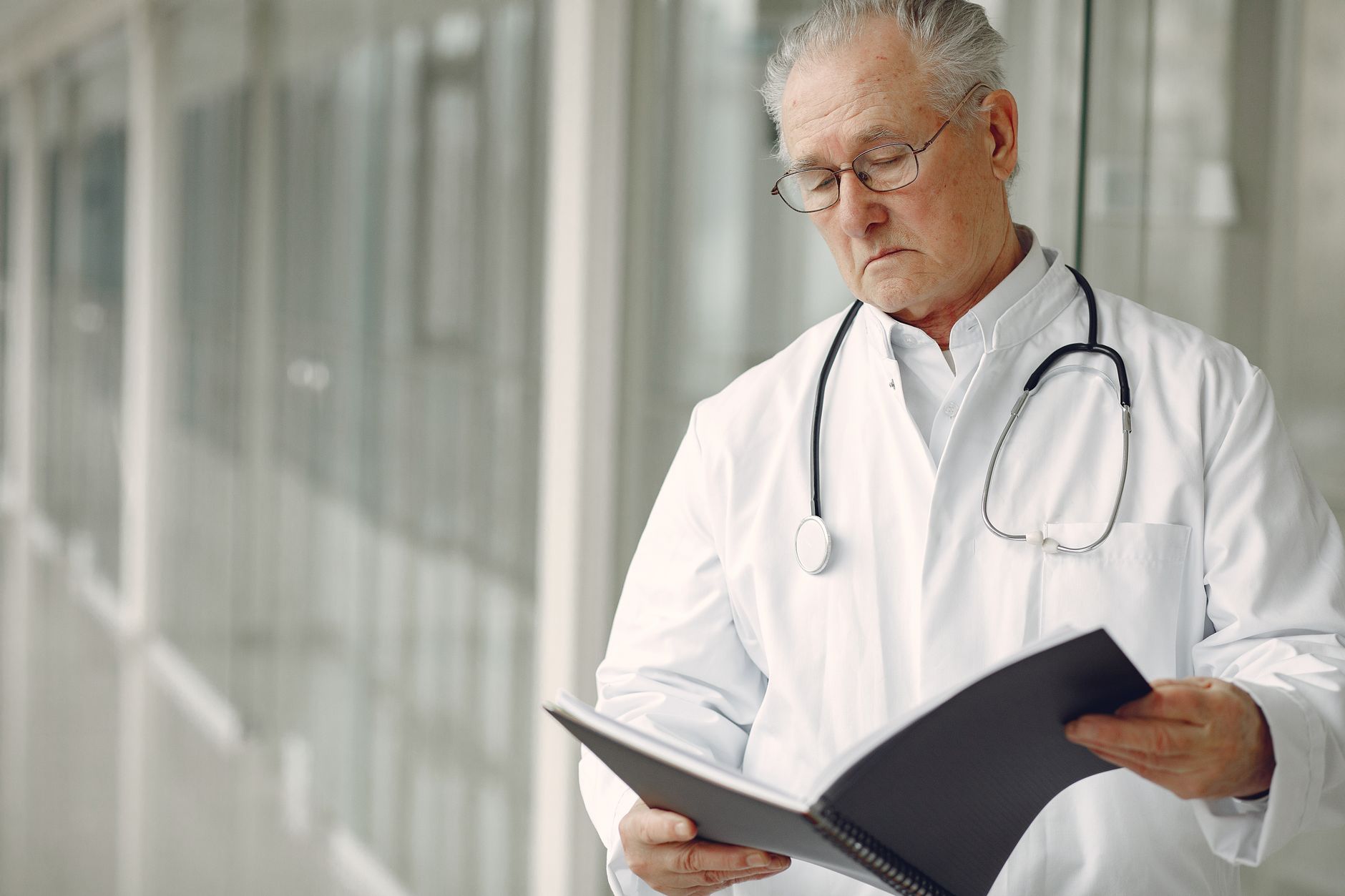 Elderly male doctor in white coat reading a patient care plan in a clinic.