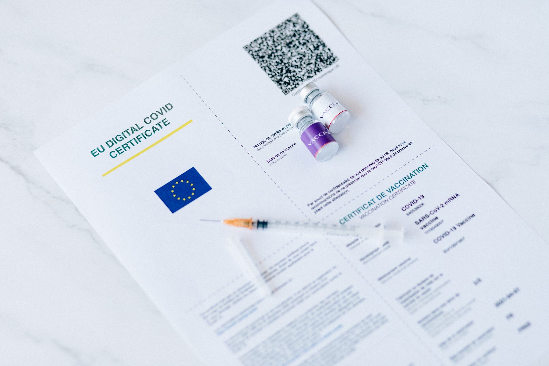 EU Digital Covid Certificate alongside vials and syringe on a marble surface.